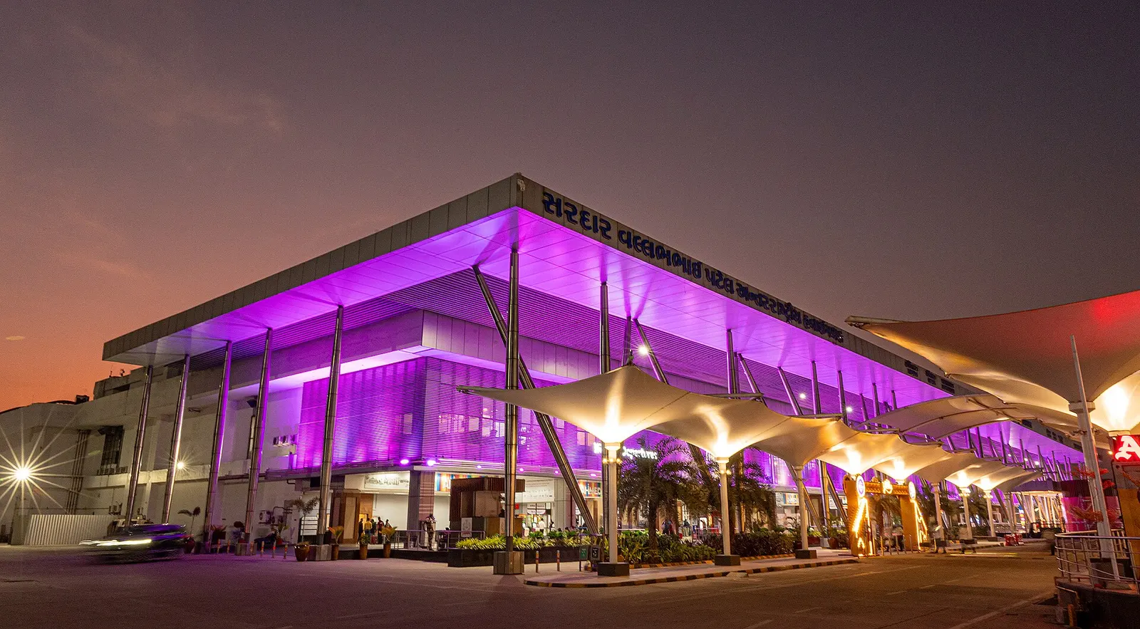 Dusk landside of Sardar Vallabhbhai Patel International Airport Terminal 1 with purple canopy lighting and tensile drop-off shades