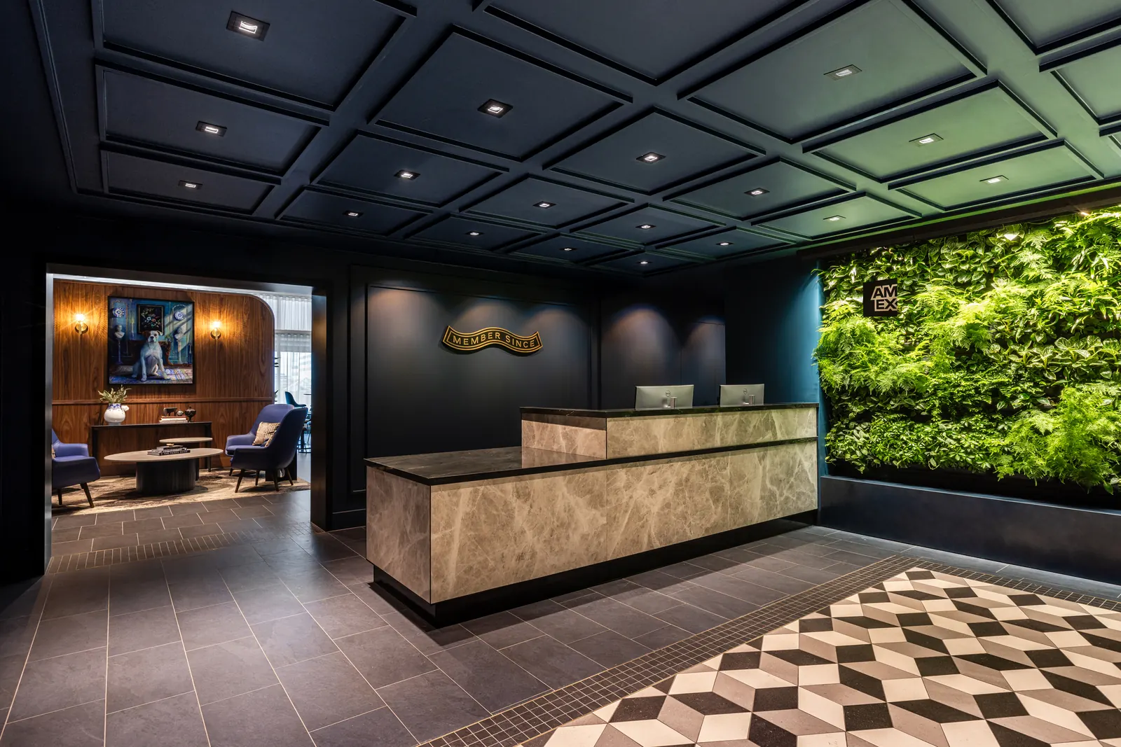 Marble reception desk with Member Since brass signage, living wall, and blue velvet seating visible through a wood-paneled doorway inside the American Express Centurion Lounge at Amsterdam Schiphol (AMS).