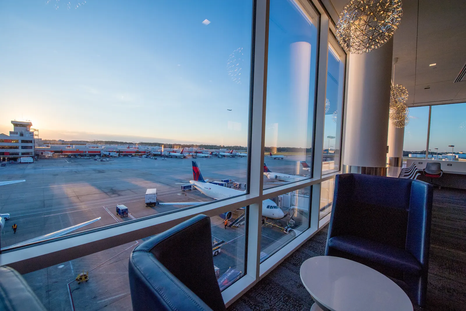 Navy armchairs and spherical pendant lights facing floor-to-ceiling windows with Delta aircraft on the apron inside the Delta Sky Club on Concourse B at Atlanta (ATL).