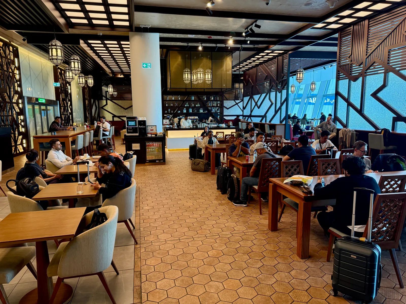 Dining tables under lantern pendants with mashrabiya-style wood lattice screens inside the Etihad Business Class Lounge at Abu Dhabi International (AUH).