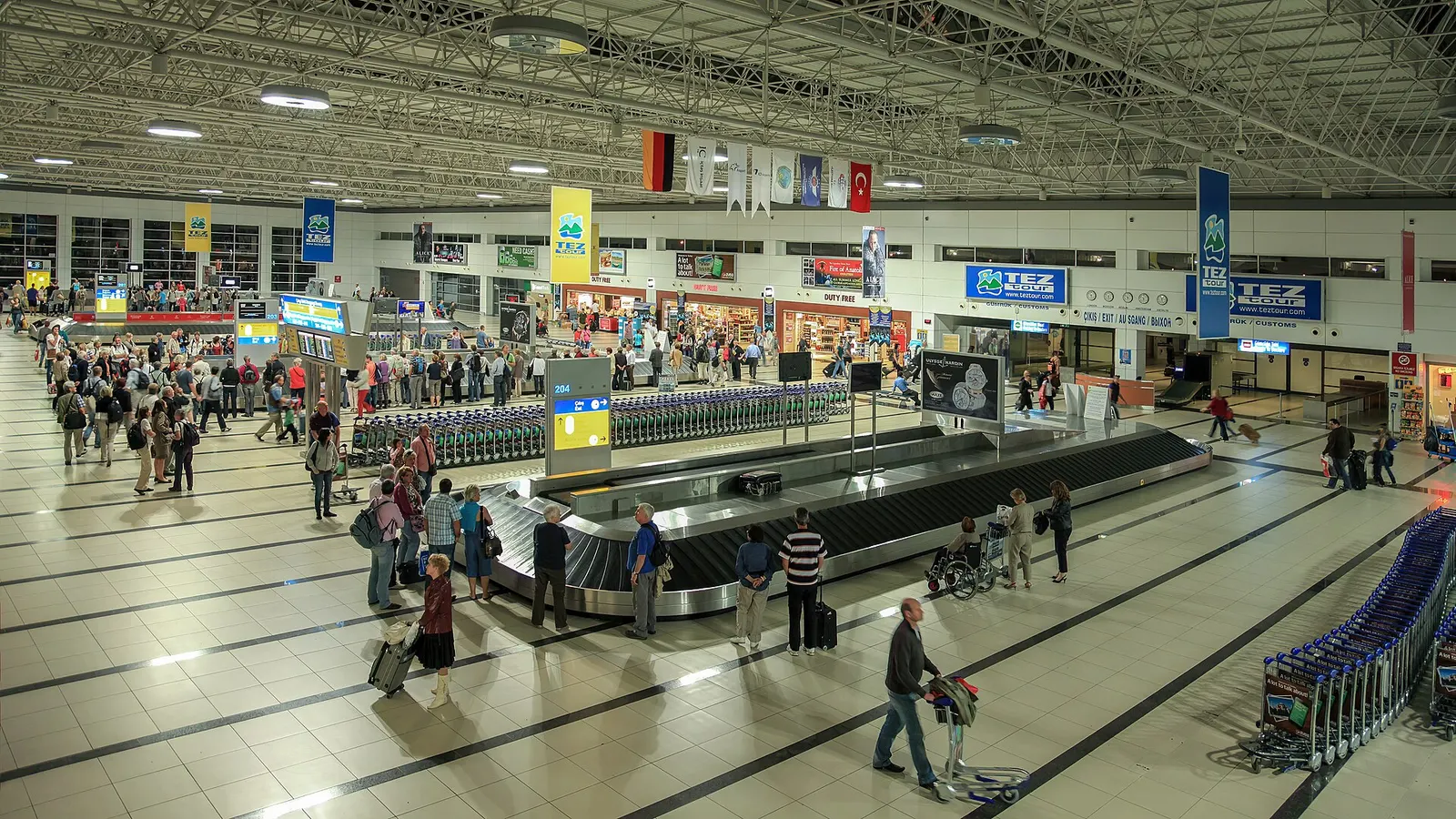 Antalya Airport baggage claim hall with multilingual exit signs and TEZ Tour banners
