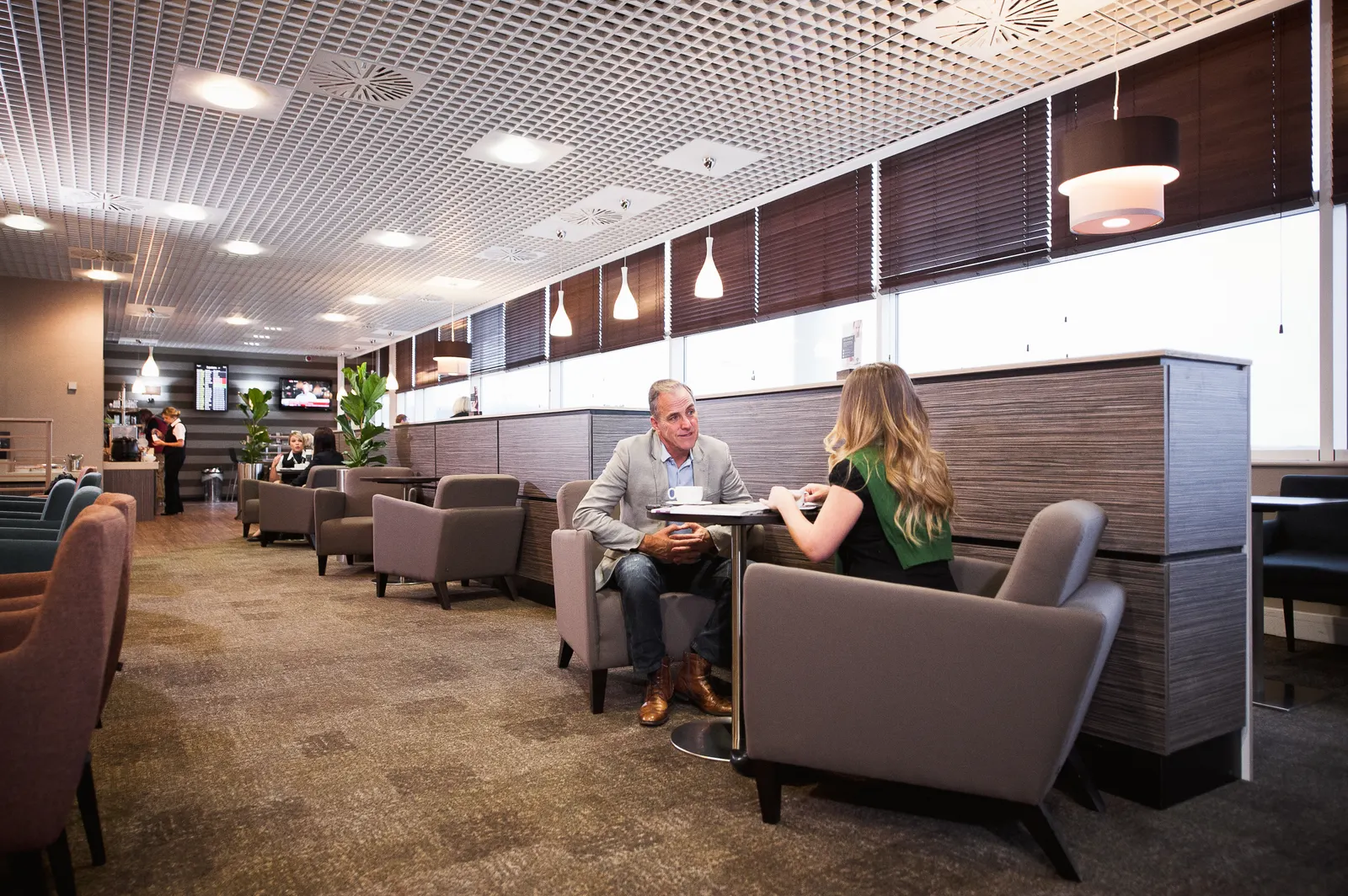 Grey and purple armchairs beside wood partitions and window blinds in Aspire Lounge South at Birmingham Airport (BHX).