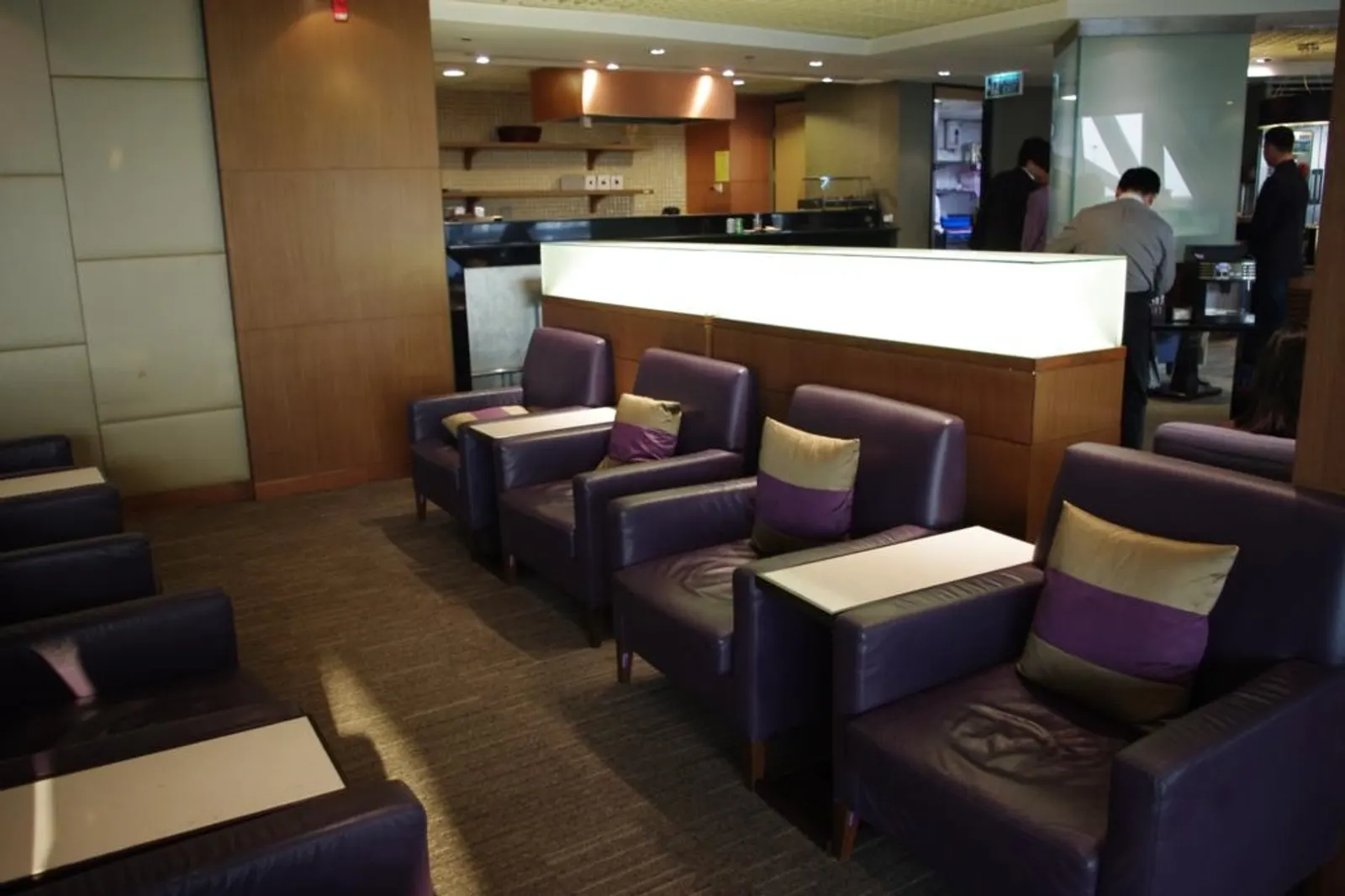 Rows of purple leather armchairs with gold-striped cushions facing a wood partition and buffet counter inside the Thai Airways Royal Silk Lounge at Suvarnabhumi (BKK).