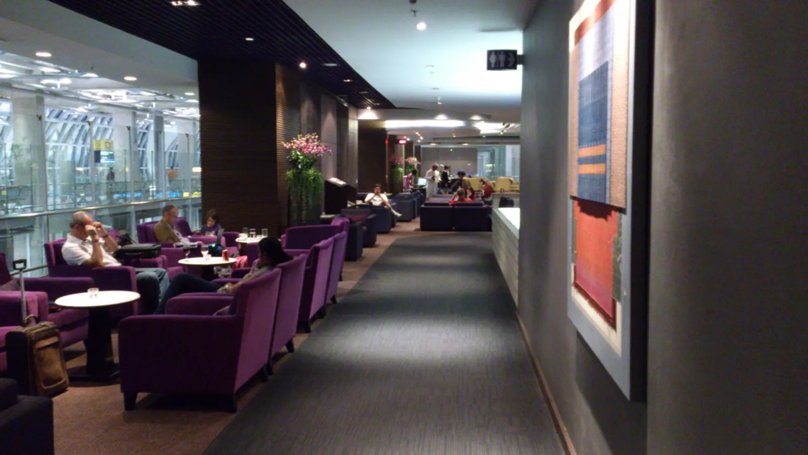 Purple lounge chairs, orchid displays, and a view toward gate D3 inside the Thai Airways Royal Orchid Club at Suvarnabhumi (BKK).
