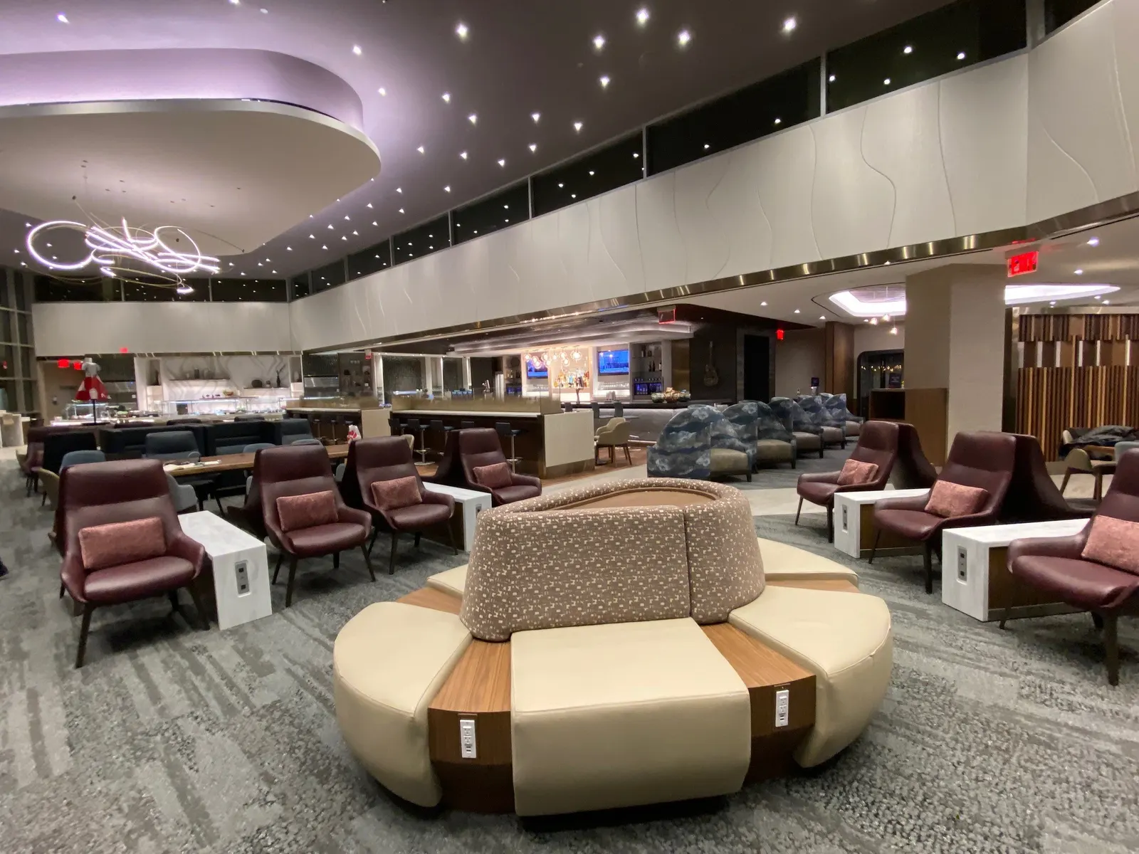 Circular ottoman, burgundy armchairs and bar beyond under purple ceiling cove in the Delta Sky Club at Nashville (BNA).