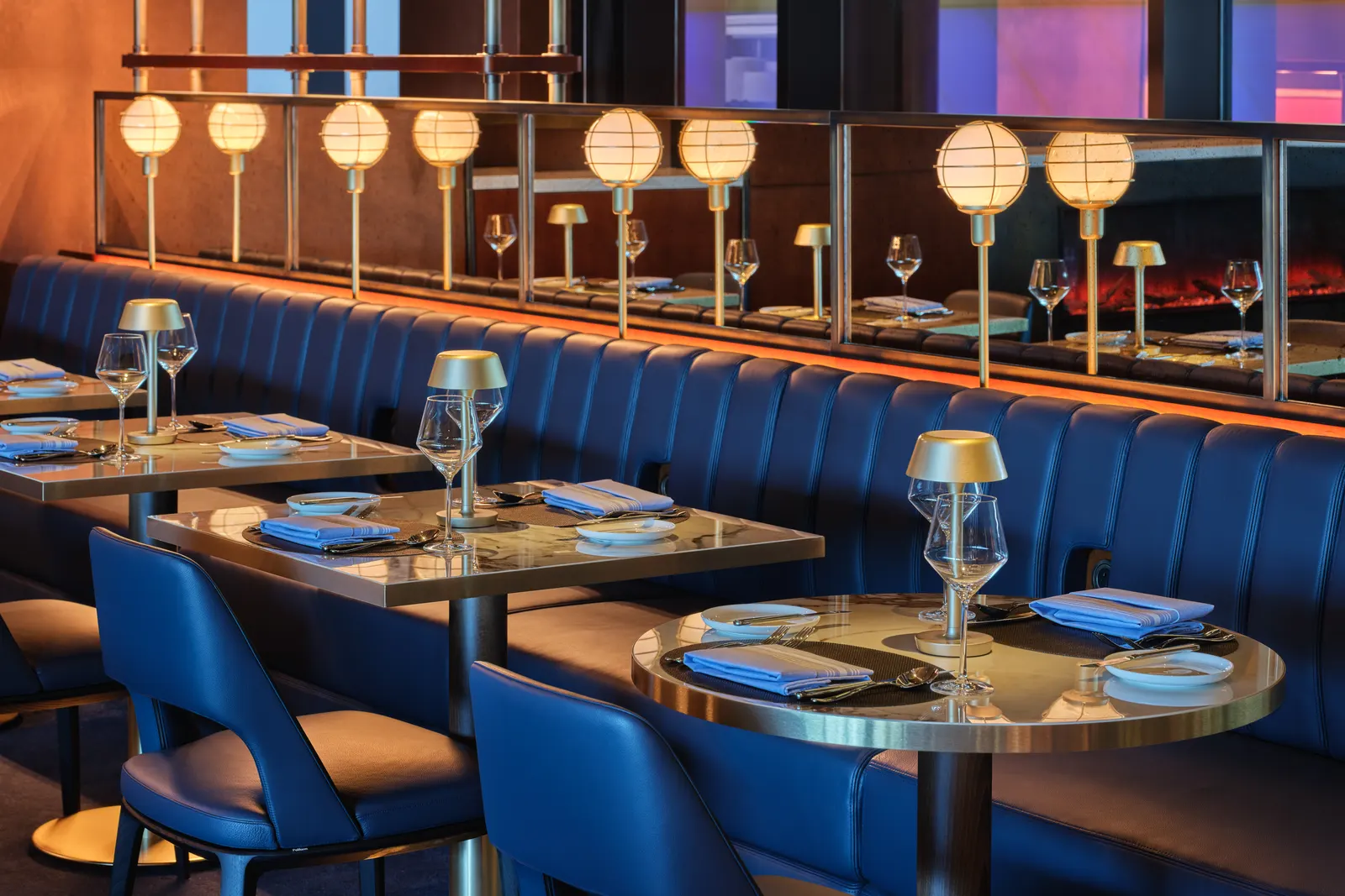 Navy tufted banquette and marble dining tables with gold task lamps in the Delta One Lounge at Boston Logan (BOS).