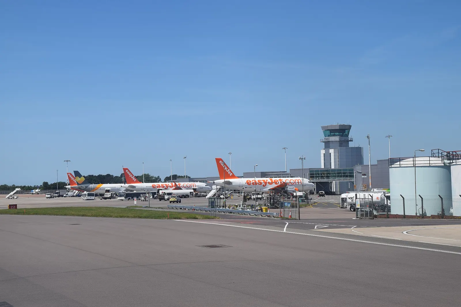 A picture of multiple EasyJet aircraft (two identified as Airbus A319-111 'G-EZAP' & Airbus A320-214 'G-EZOG' respectively) and a Thomas Cook Airlines Airbus A321-211 registered as G-TCDH parked at Bristol (Lulsgate) Airport, 19 June 2017, showing the new terminal and control tower (built in stages