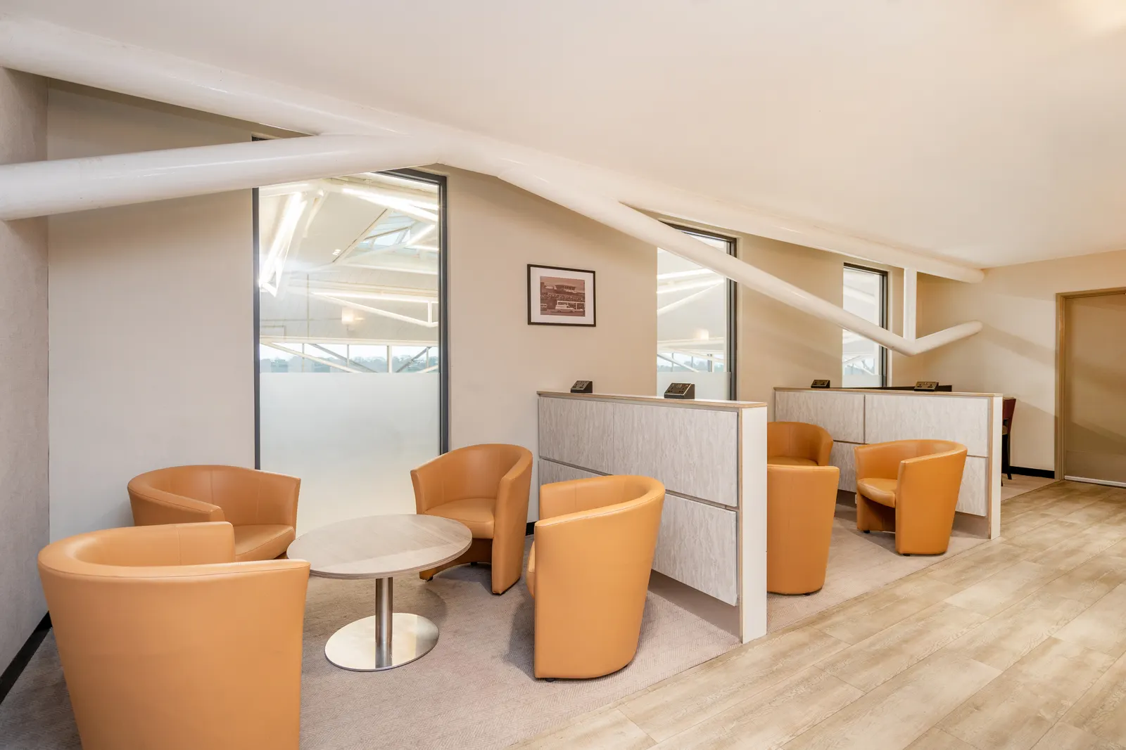 Burnt-orange tub chairs around a round table with white work pods behind in Essence by Escape Lounges at Bristol Airport (BRS).