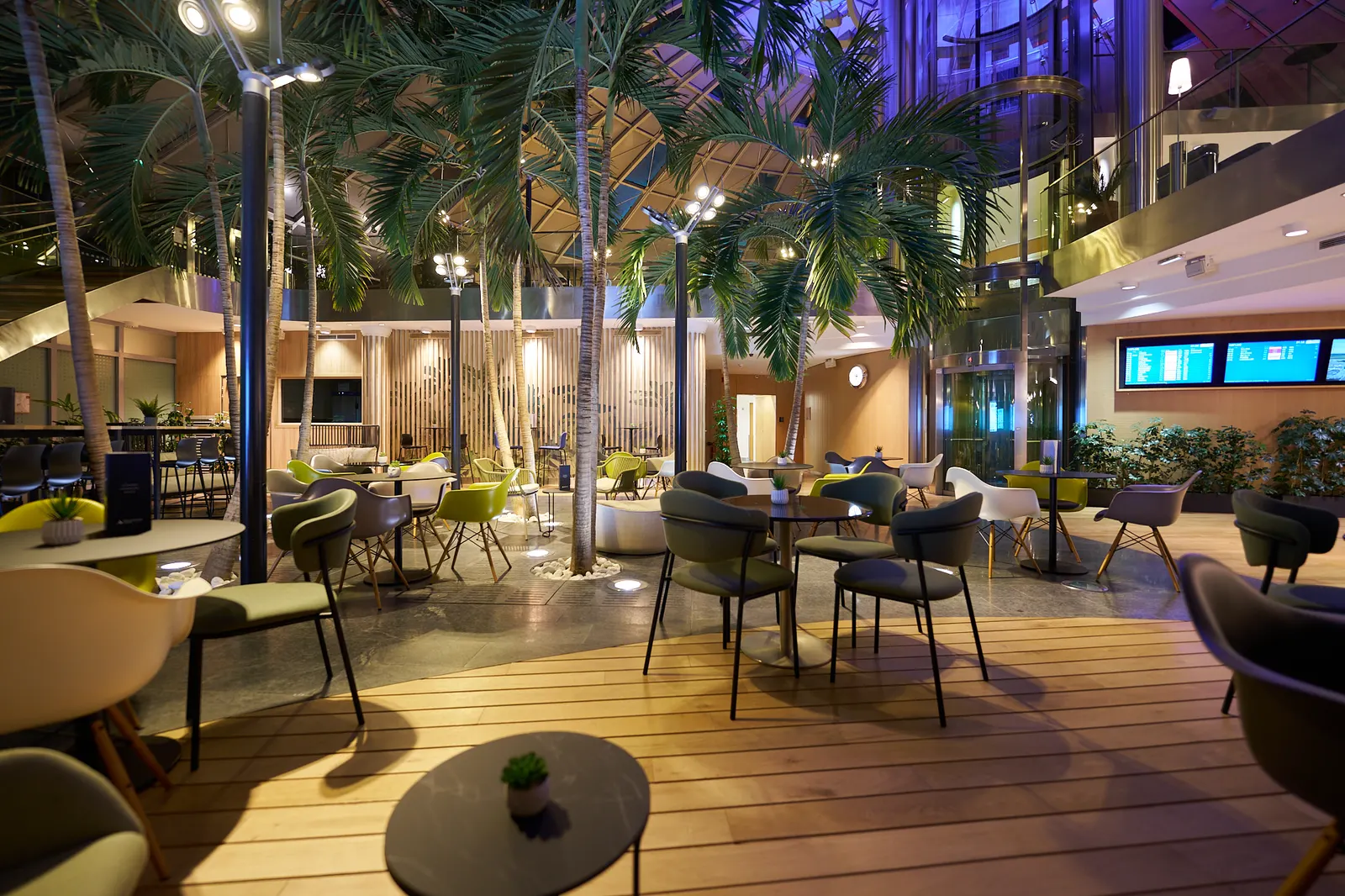Armchairs and coffee tables with flight screens beyond in Sky Cafe by Aspire at EuroAirport Basel-Mulhouse-Freiburg (BSL).