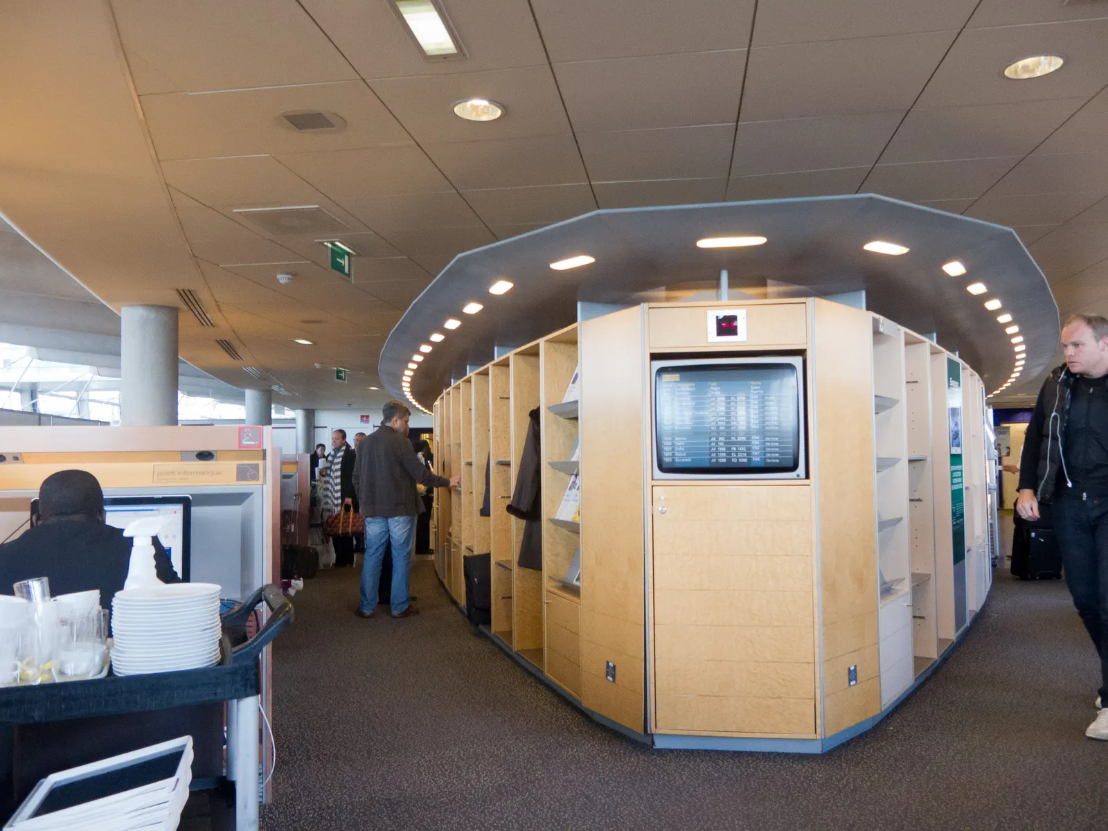 Curved wooden coat cubbies with an embedded flight-information screen inside the Air France Lounge at Paris Charles de Gaulle Terminal 2E (CDG).