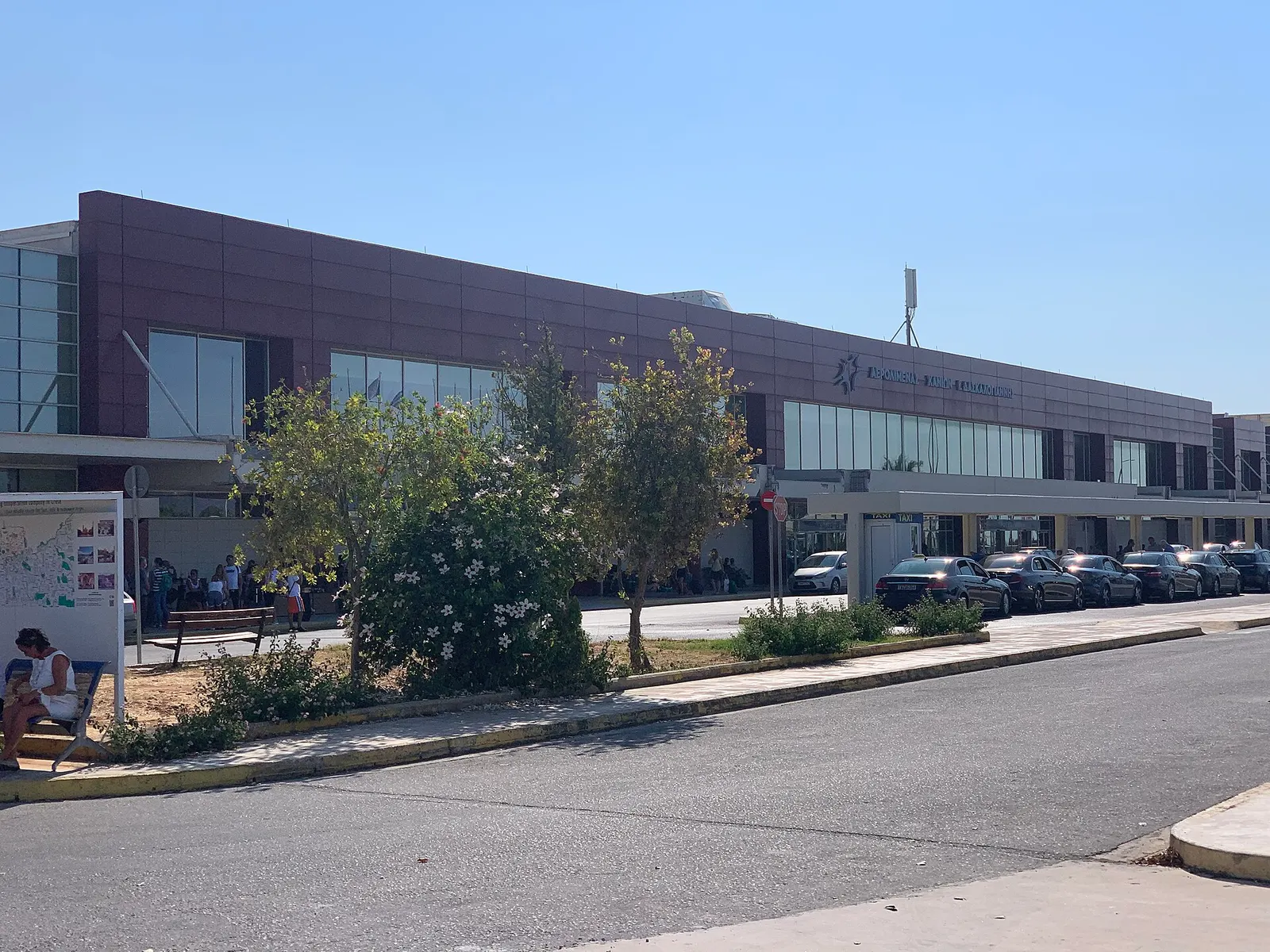 White terminal building with a red Chania sign, seen from the landside road in July 2021.
