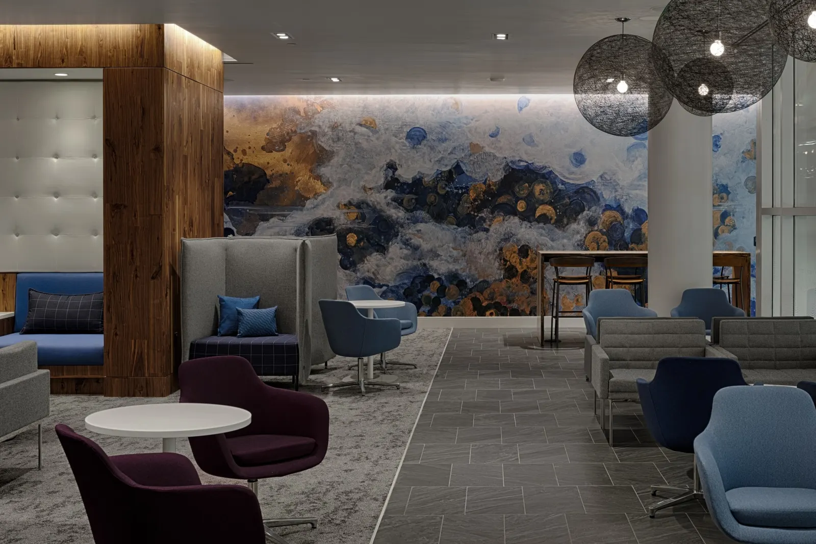 High-back sofa and purple armchairs in front of a colorful abstract mural near floor-to-ceiling windows in the Centurion Lounge at Charlotte Douglas (CLT).
