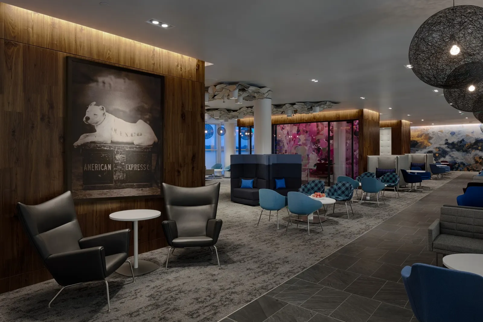 Leather and blue armchairs around low tables beneath mesh pendant lights and a Centurion watchdog artwork in the Centurion Lounge at Charlotte Douglas (CLT).