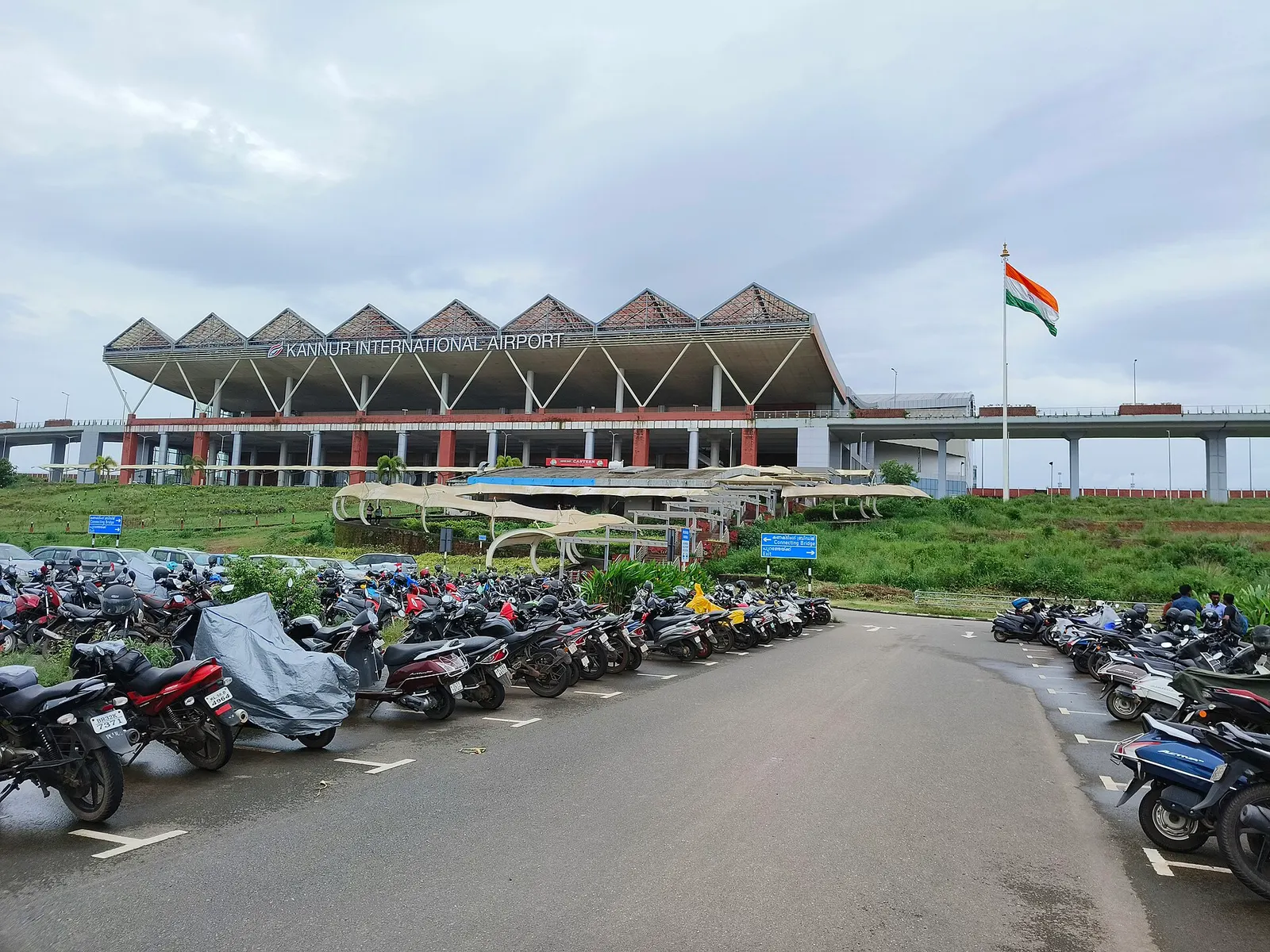 Landside forecourt of Kannur International Airport on 5 July 2025, with the curved terminal roof and a row of parked cars