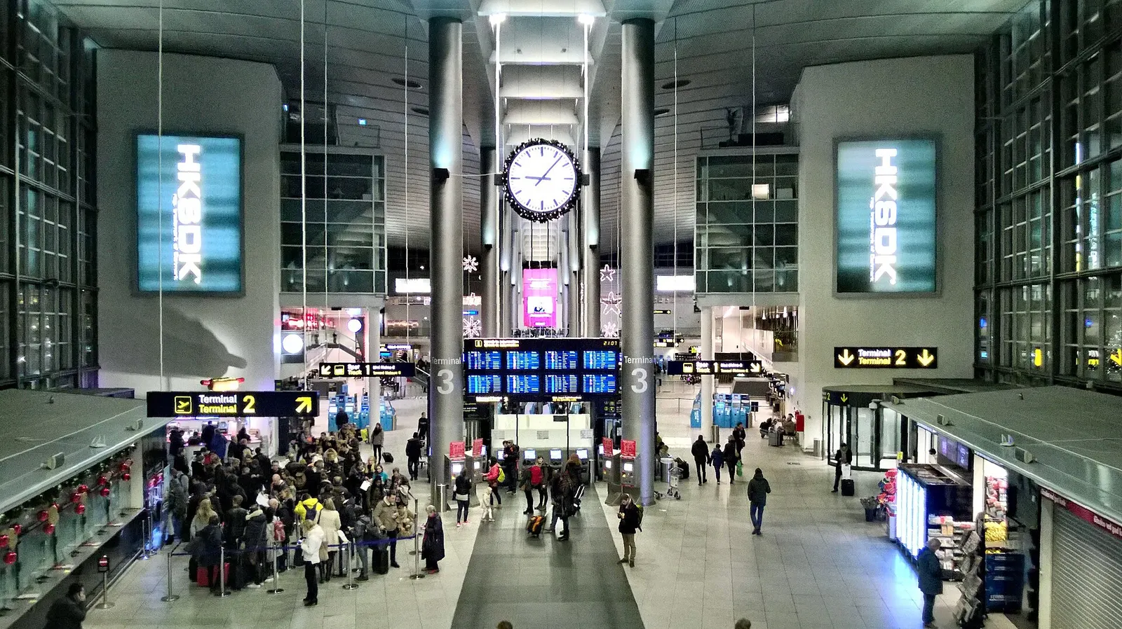 Copenhagen Airport check-in hall with Terminal 2 and Terminal 3 signs, clock, and queue.