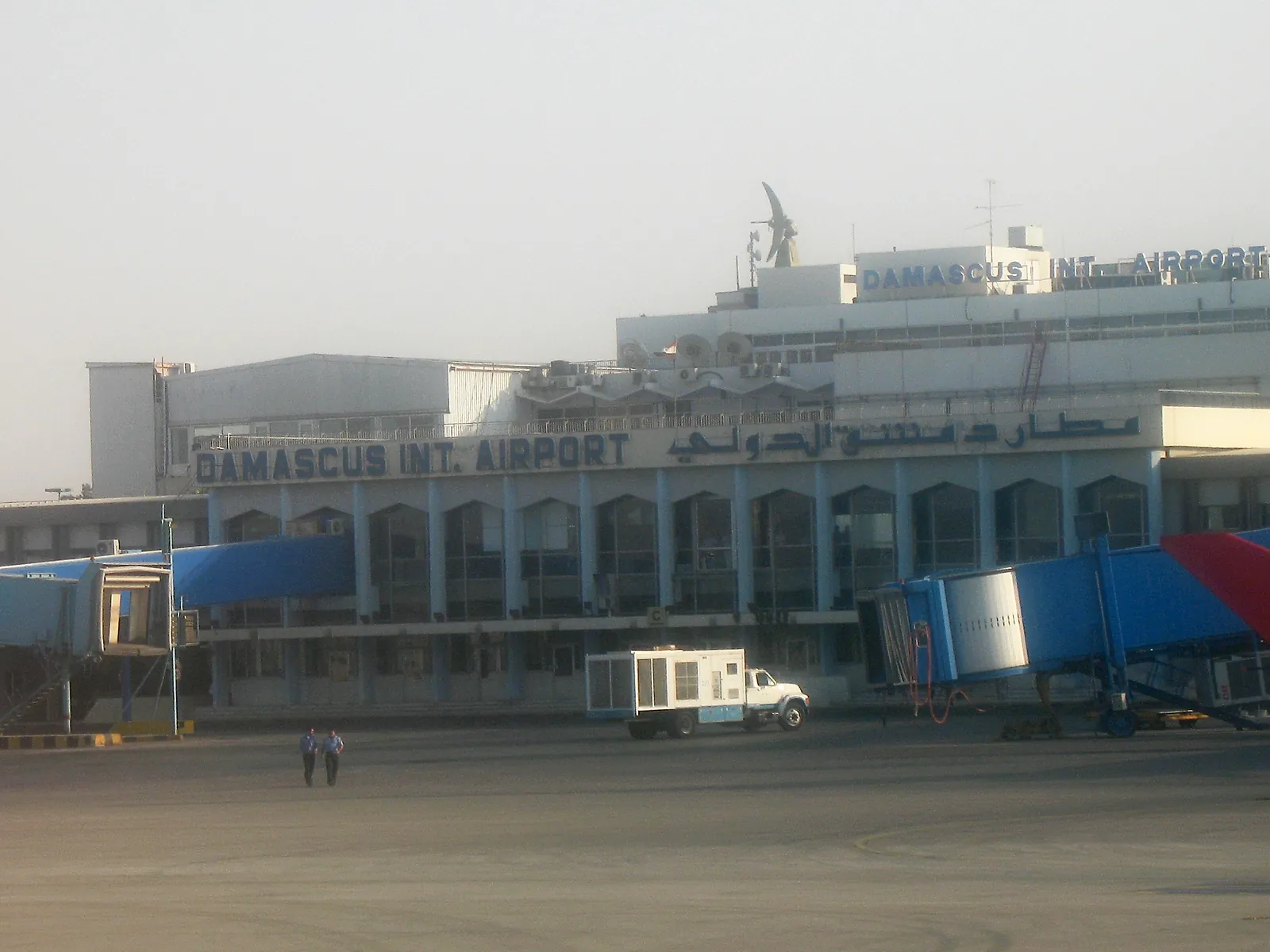 Airside side of the Damascus International Airport terminal with jet bridges and the 'Damascus Int. Airport' sign