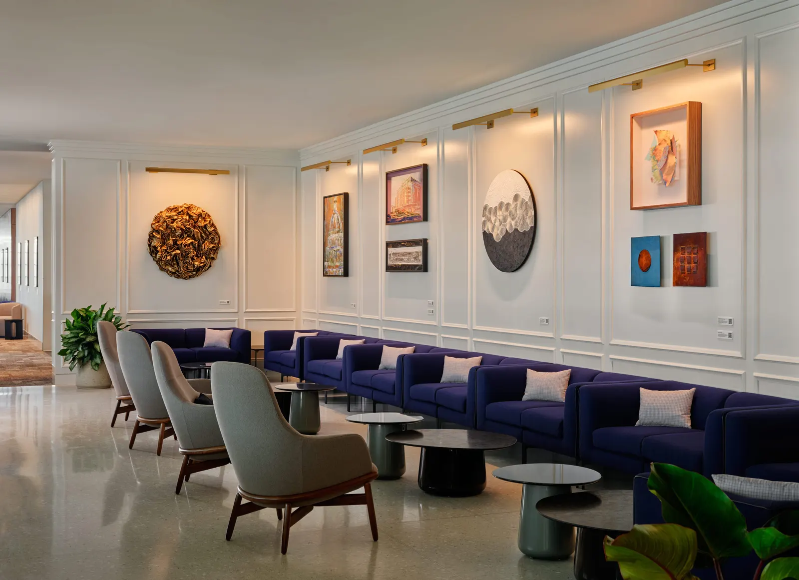 Long navy banquette with cushions and grey armchairs beneath a wall of locally commissioned artwork in the Centurion Lounge at Ronald Reagan Washington National Airport (DCA).