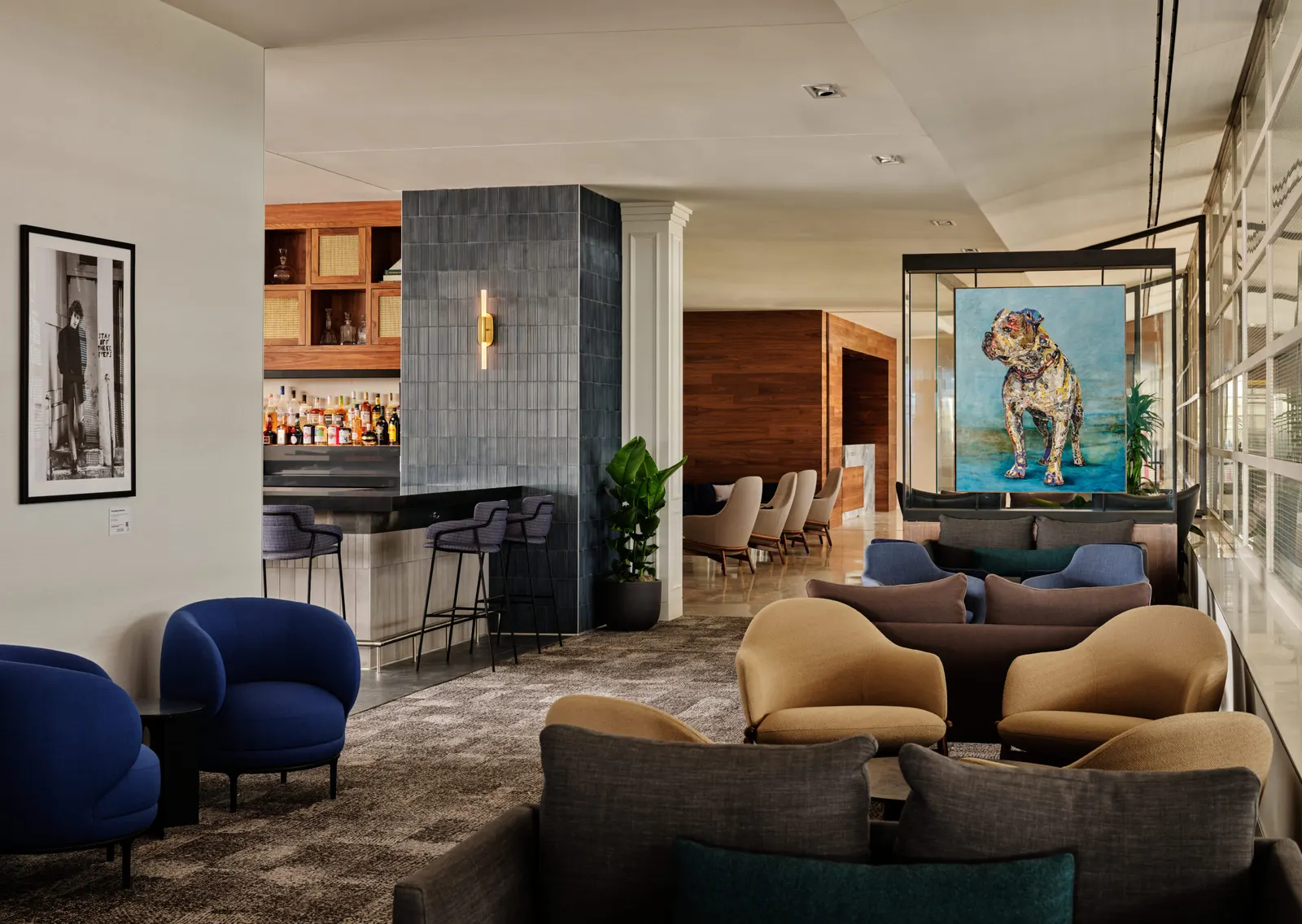 Tan and navy armchairs grouped around low tables near a glass-encased dog artwork and a bar counter in the Centurion Lounge at Ronald Reagan Washington National Airport (DCA).