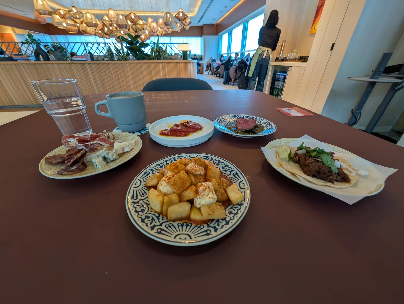 Tapas plates on a dining table with clustered lantern lighting and lounge seating beyond inside Capital One Landing at Ronald Reagan Washington National (DCA).