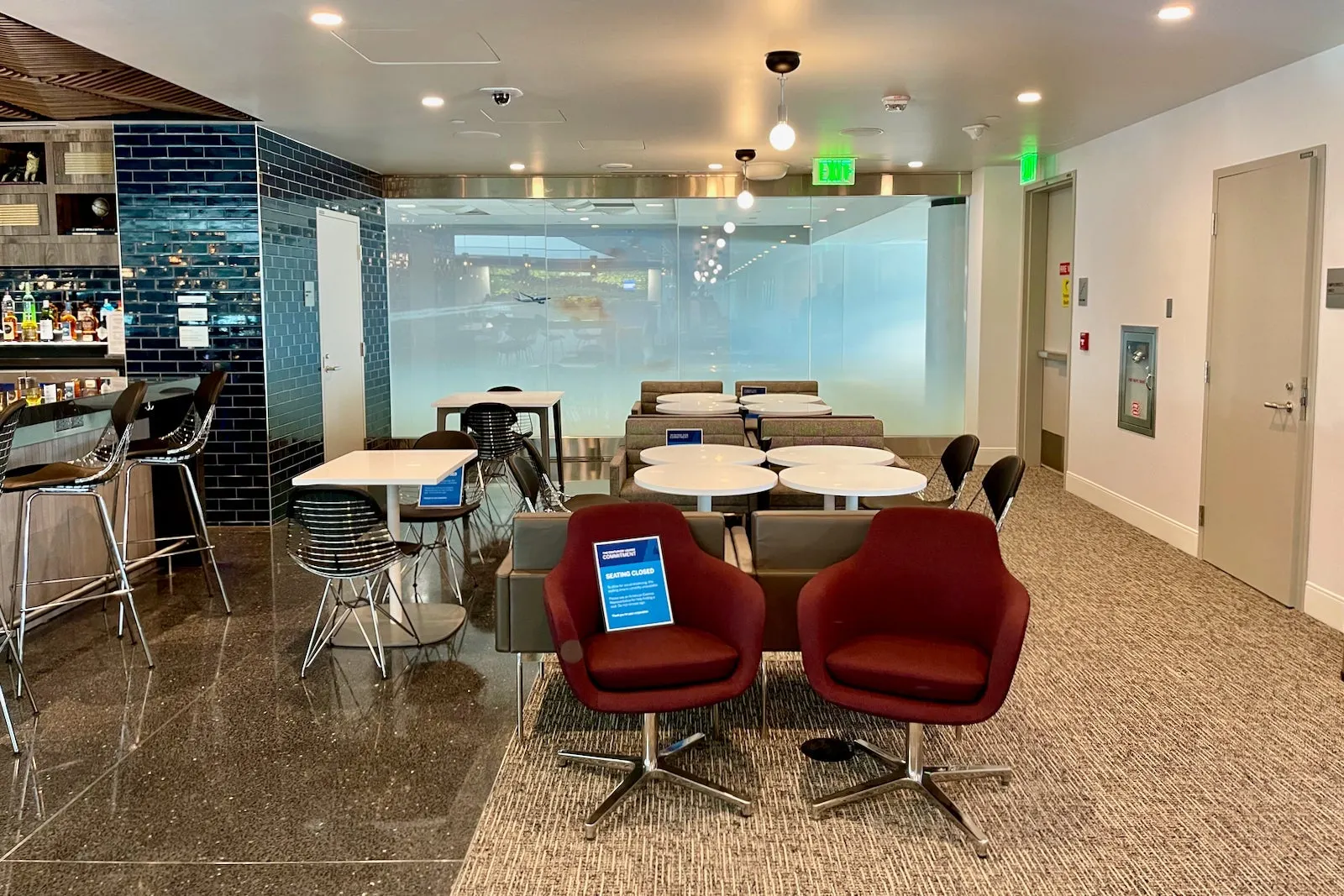 Maroon swivel chairs and wire dining seats near the navy-tiled bar in The Centurion Lounge at Denver International Airport (DEN).