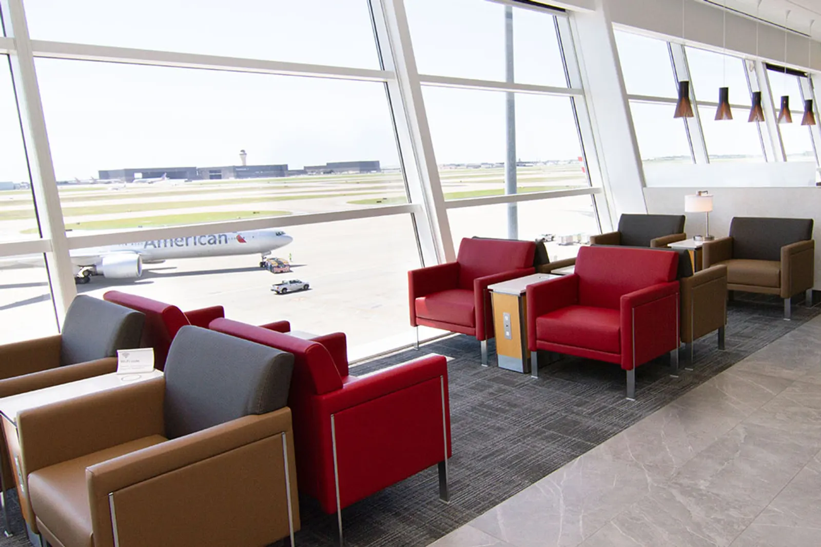Red and grey armchairs with apron views in the American Airlines Flagship Lounge at Dallas Fort Worth International Airport (DFW).