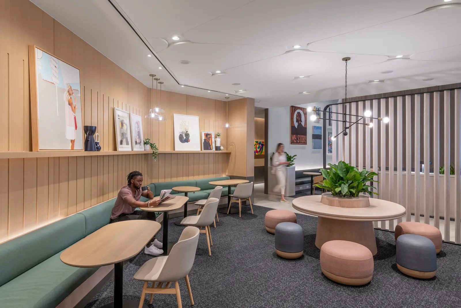 Teal banquette with wood tables, round ottomans and a planter table beneath wall art in the Capital One Lounge at Dallas Fort Worth Terminal D (DFW).