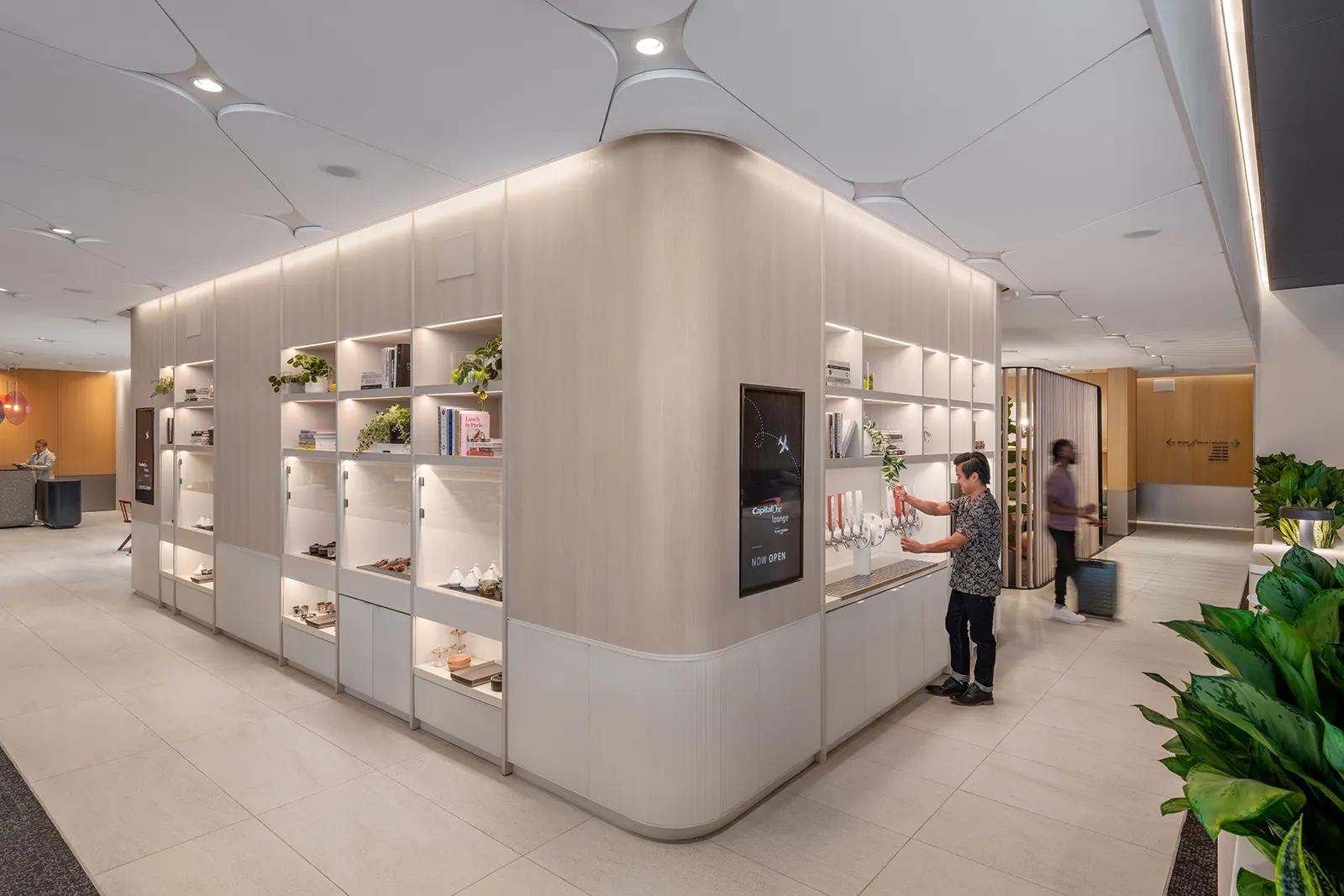 Curved white grab-and-go market shelving with packaged snacks and drinks in the Capital One Lounge at Dallas Fort Worth Terminal D (DFW).