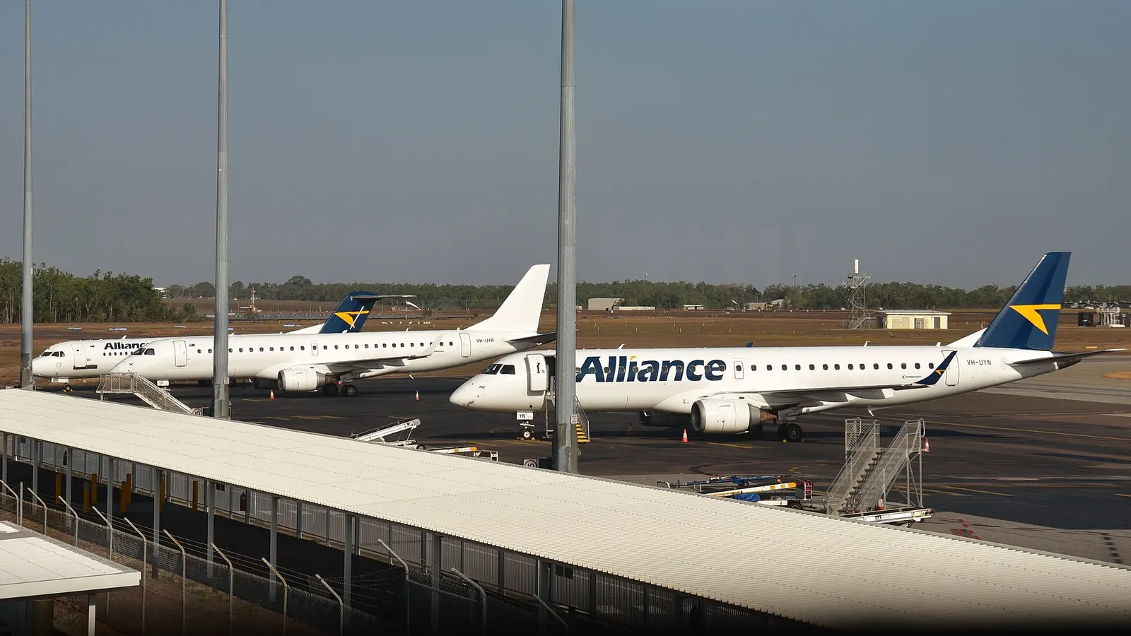 A lineup of narrow bodied Alliance Airlines airliners at Darwin International Airport (DRW/YPDN), Australia – from left to right are Fokker 100 VH-UQN, Embraer 190AR VH-UYR, and Embraer 190AR VH-UYN