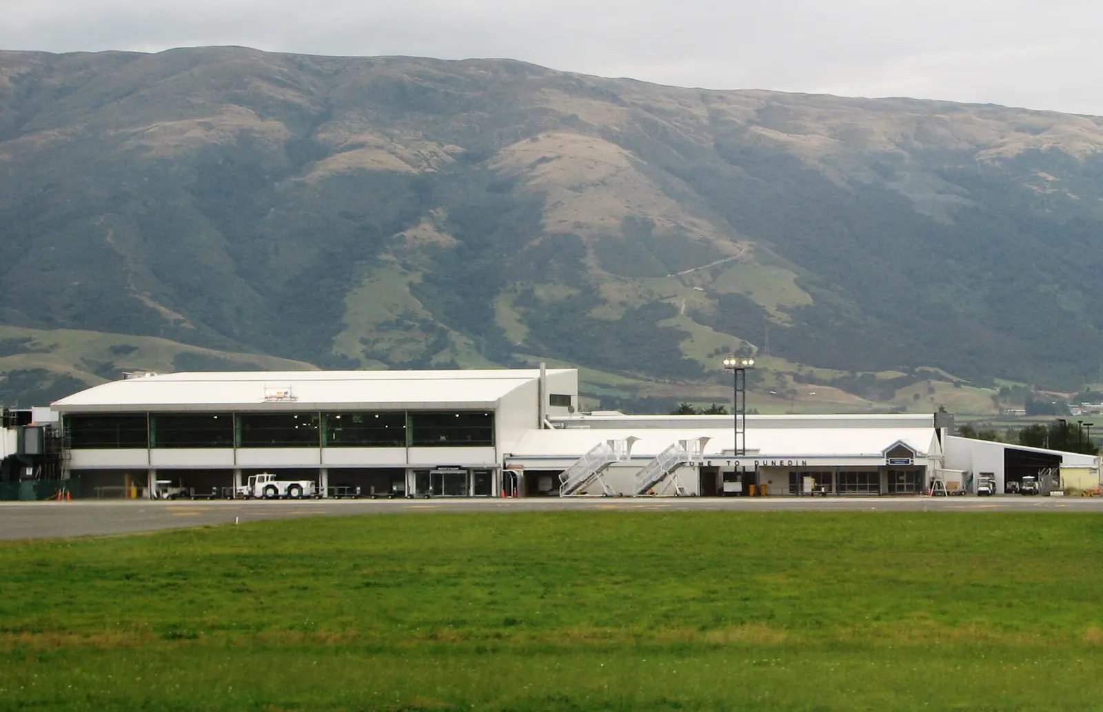Dunedin International Airport seen from the runway. The airport is situated in a valley between green hillsides.