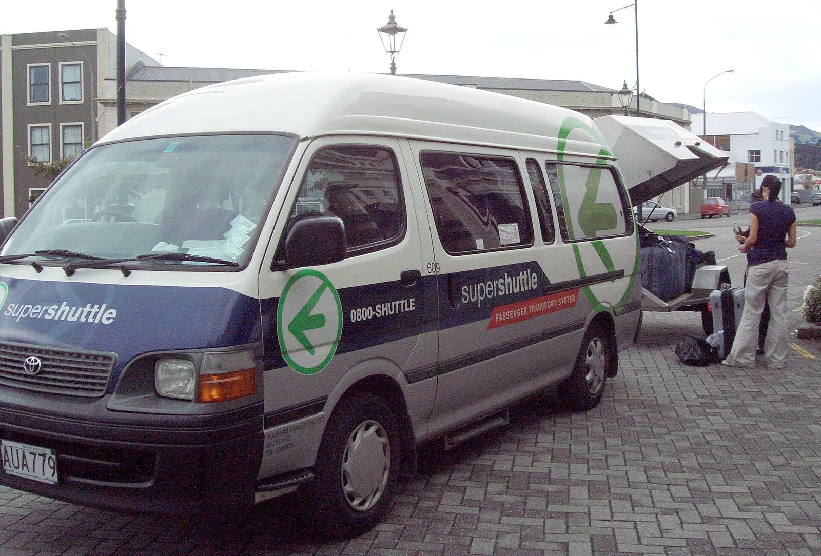 Super Shuttle van operated by Tourism Holdings Ltd subsidiary Tourism Transport providing shared taxi service to Dunedin Airport from Dunedin Railway Station forecourt.