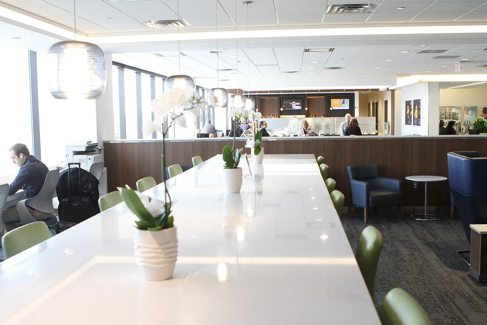 Long white communal work table with lime-green chairs and hanging glass pendants in the Delta Sky Club at Newark (EWR).