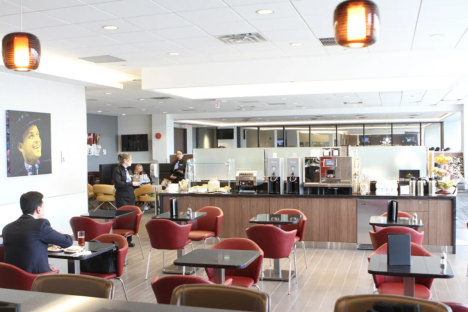 Dining tables with red chairs and a buffet counter in the Delta Sky Club at Newark (EWR).