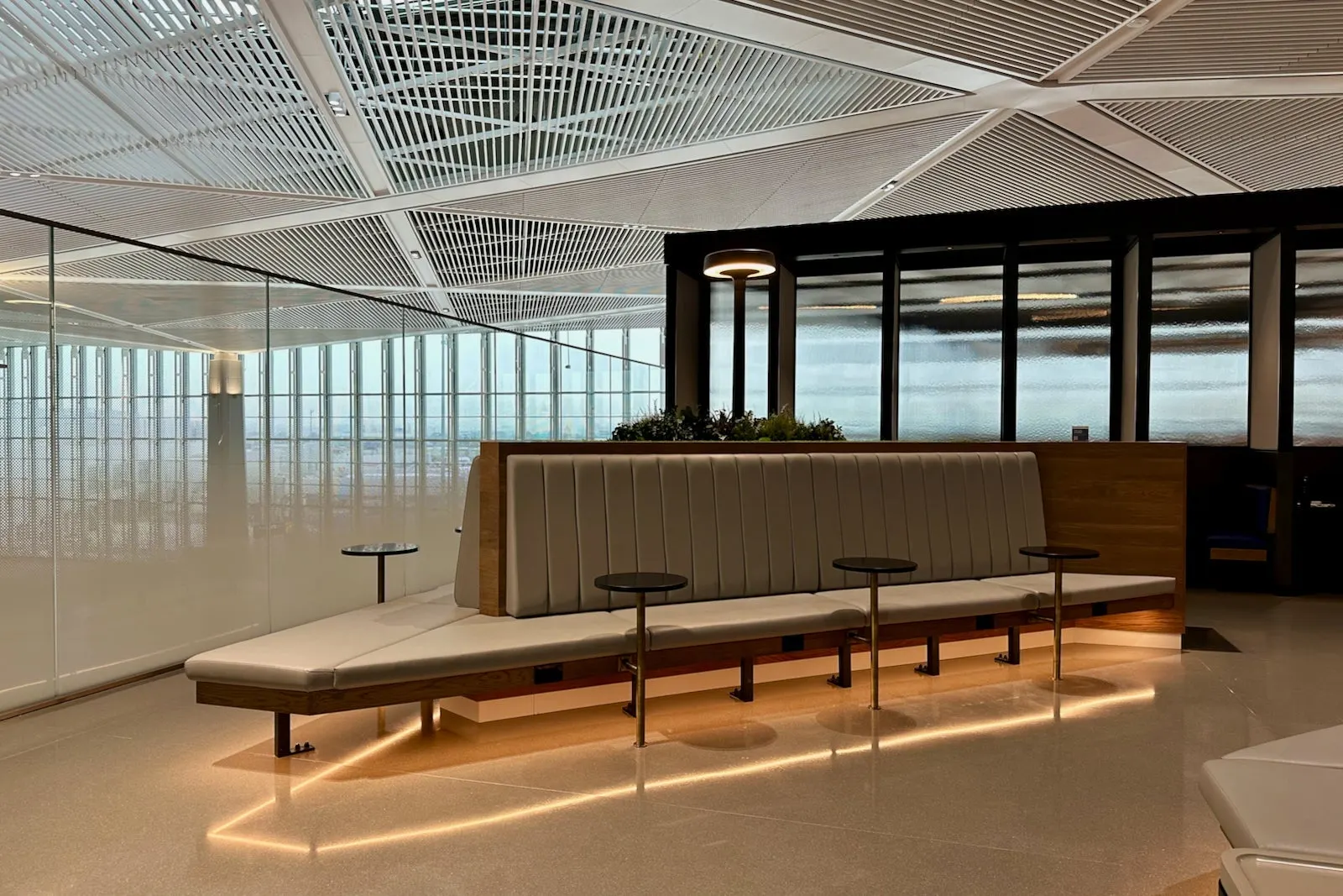 Light grey ribbed banquette with round pedestal tables and planter divider in the United Club at Newark Terminal A.