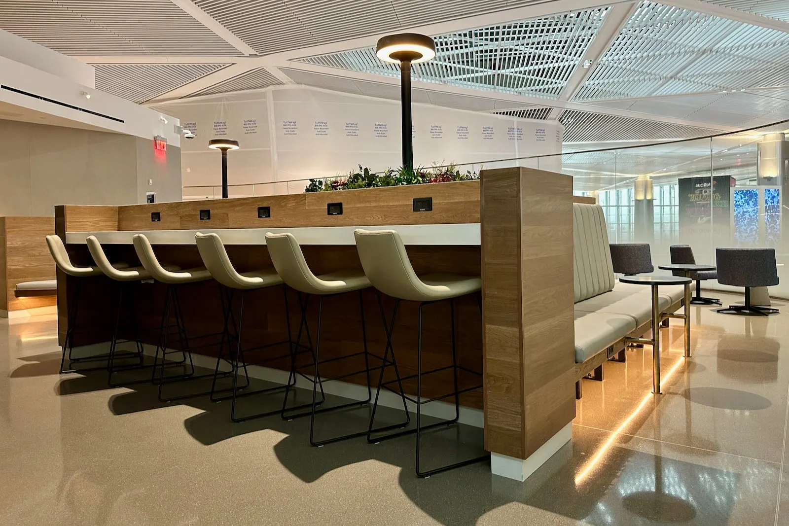 Wood high-top table with beige barstools and ring floor lamps in the United Club at Newark Terminal A.