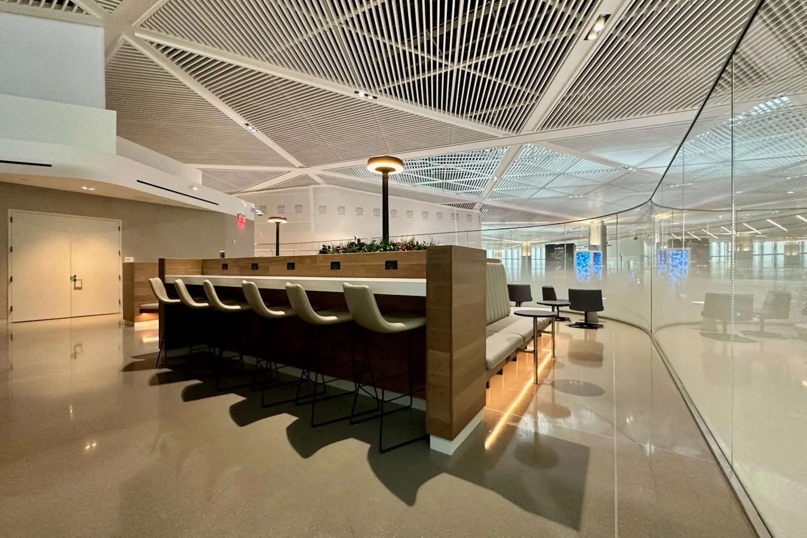 Wood workspace island with barstools and banquette under geometric ceiling in the United Club at Newark Terminal A.