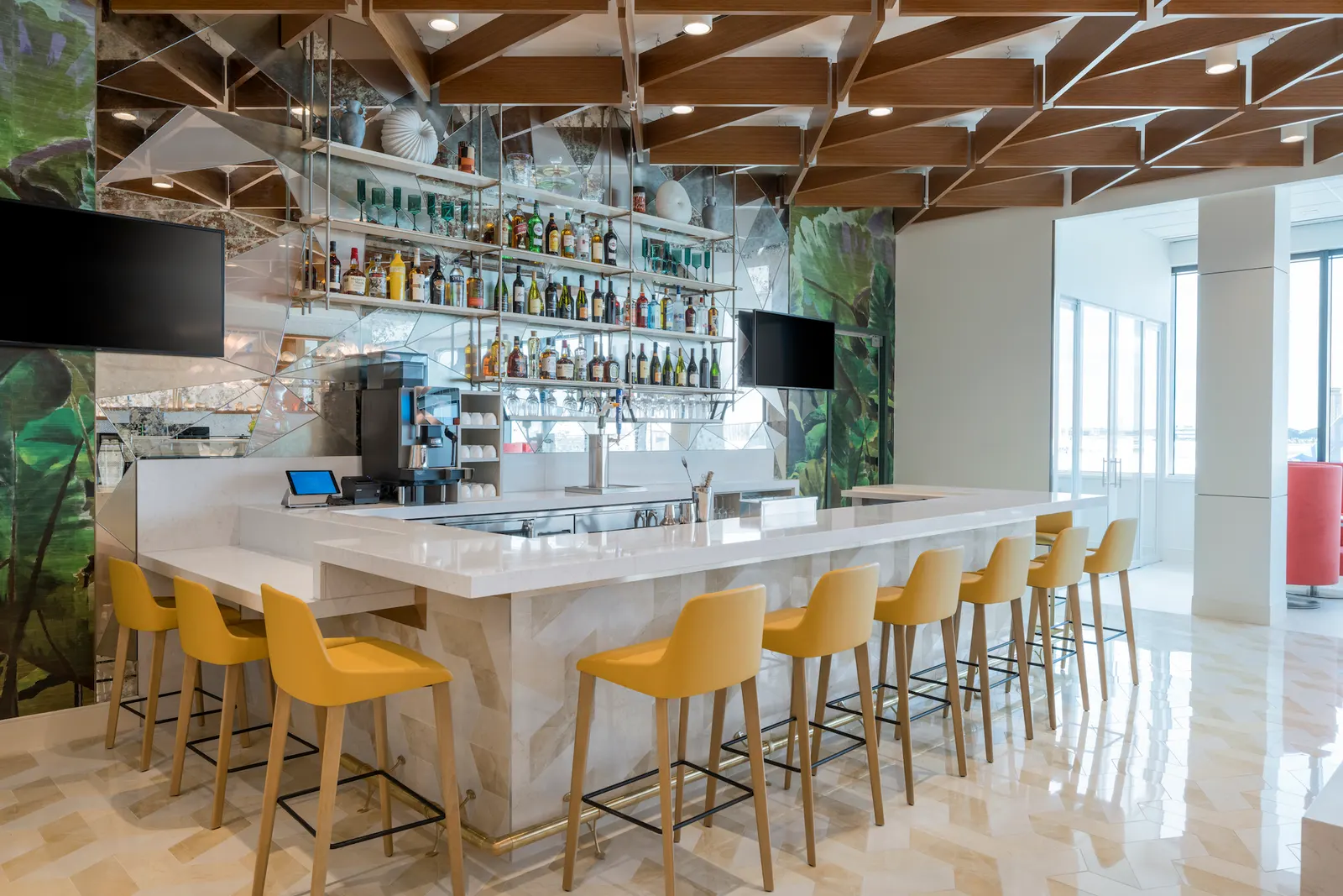 L-shaped bar with yellow bucket stools, botanical wallpaper and wood lattice ceiling in the Escape Lounges at Fort Lauderdale (FLL).