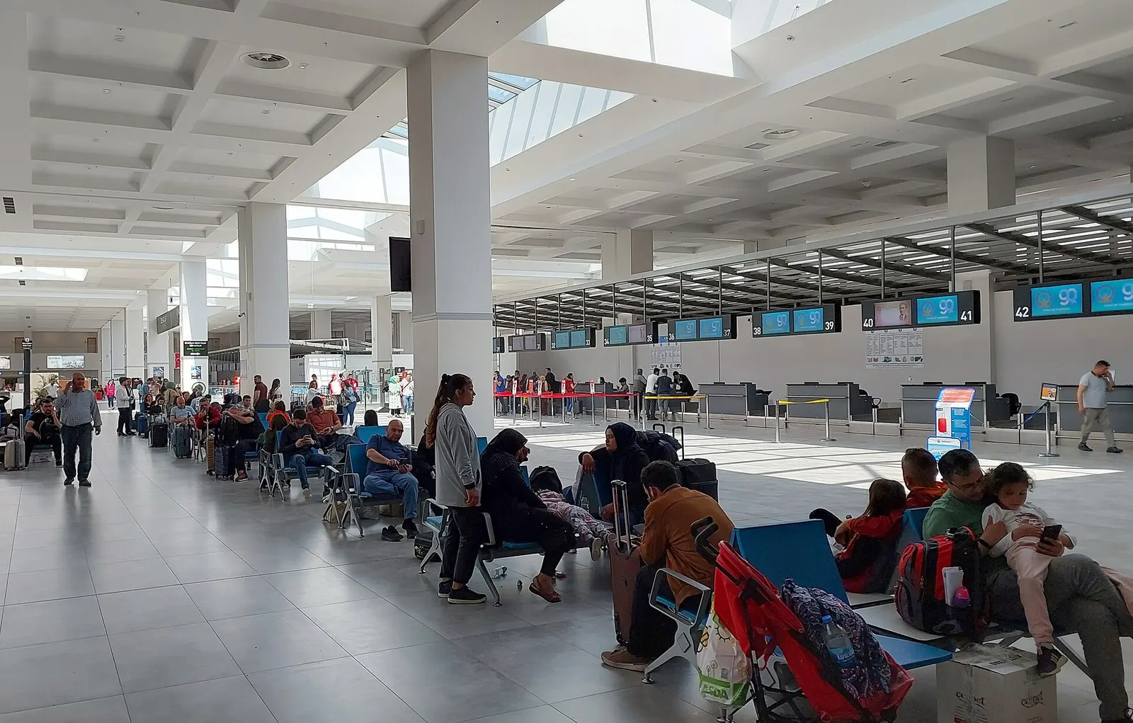 Check-in hall of Gaziantep Oğuzeli Airport, with a high ceiling, ticket desks, and travelers in the 2021 passenger terminal.