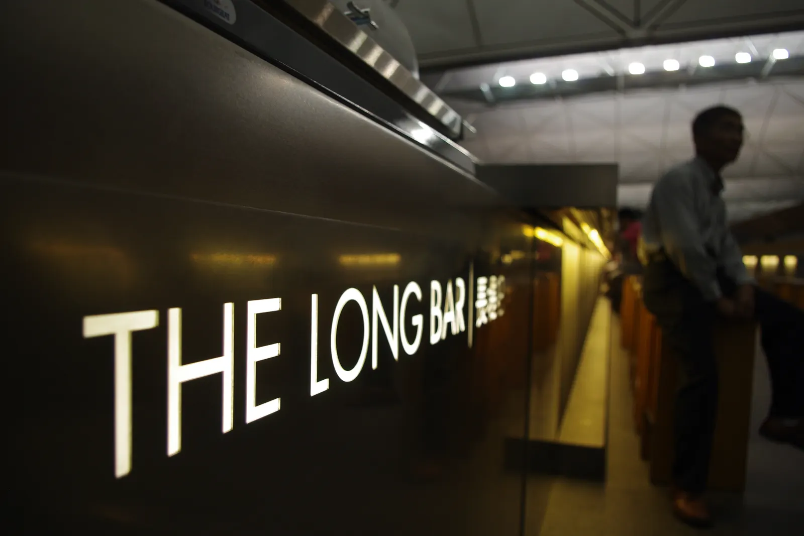 Illuminated THE LONG BAR signage on the bar face inside Cathay Pacific The Wing at Hong Kong International (HKG).