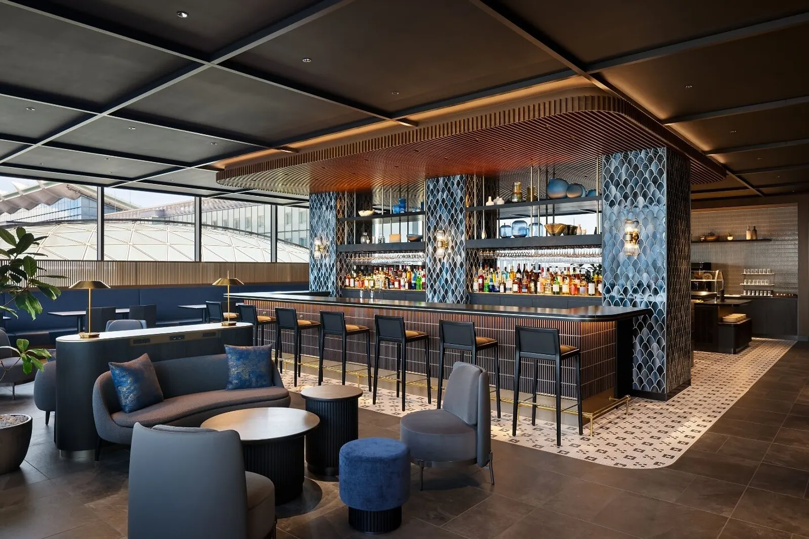 Curved wood-slat bar with blue scalloped tile columns and lounge seating beside airfield windows in the Centurion Lounge at Haneda (HND).