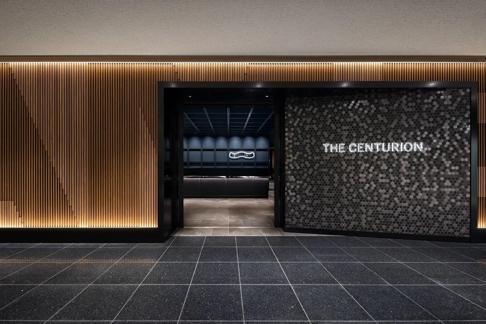 Centurion Lounge entrance with illuminated THE CENTURION lettering on hexagonal tile beside a glowing wood-slat wall at Haneda Terminal 3 (HND).