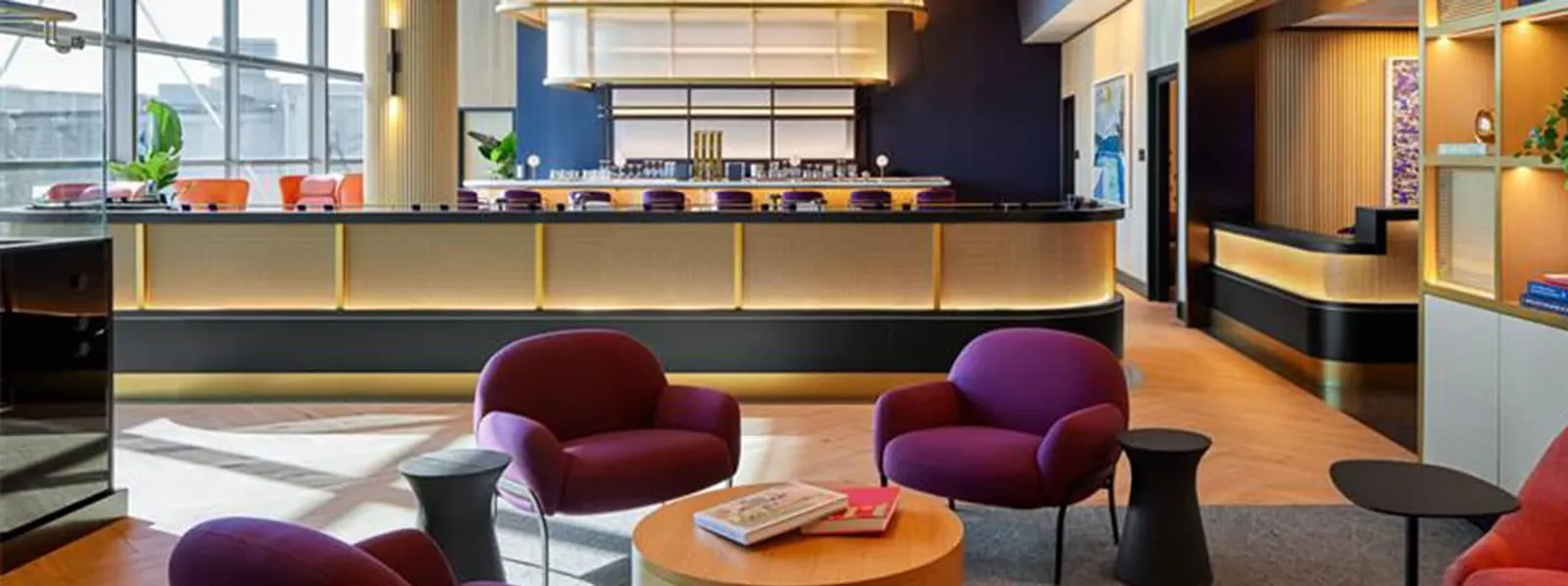 Purple armchairs around a low table in front of a long illuminated bar counter in The Etihad Lounge in collaboration with Chase at Washington Dulles Concourse A (IAD).