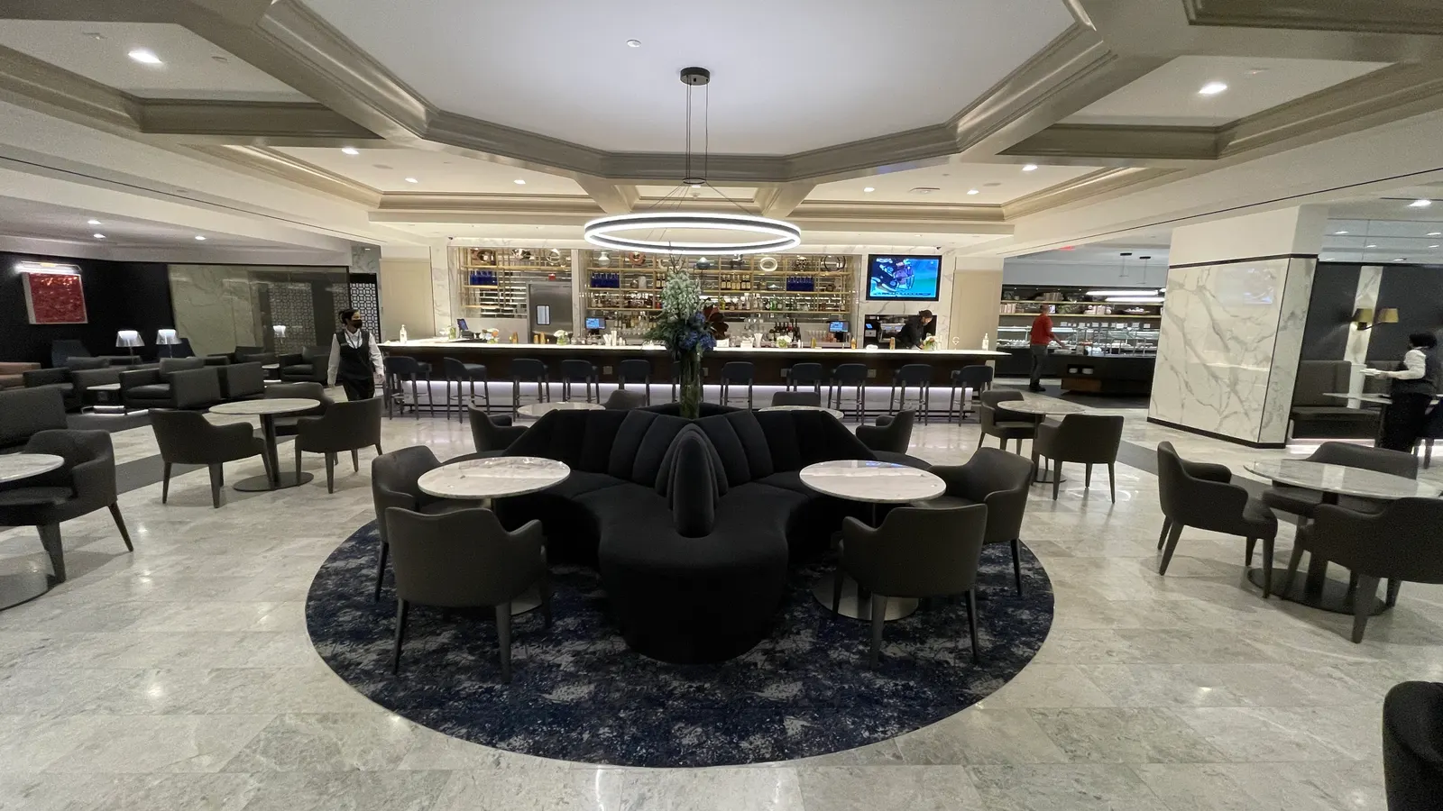 Circular banquette seating, marble tables, and a long illuminated bar inside the United Polaris Lounge at Dulles International (IAD).