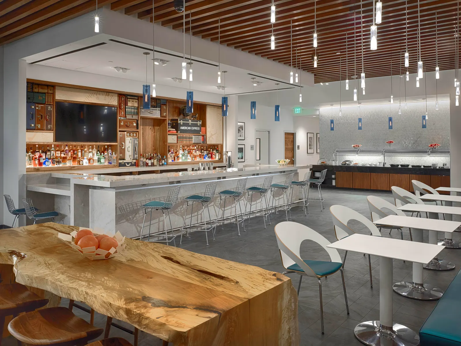 Live-edge communal table, white dining chairs and a marble bar with pendant lights in the Centurion Lounge at Houston Intercontinental (IAH).