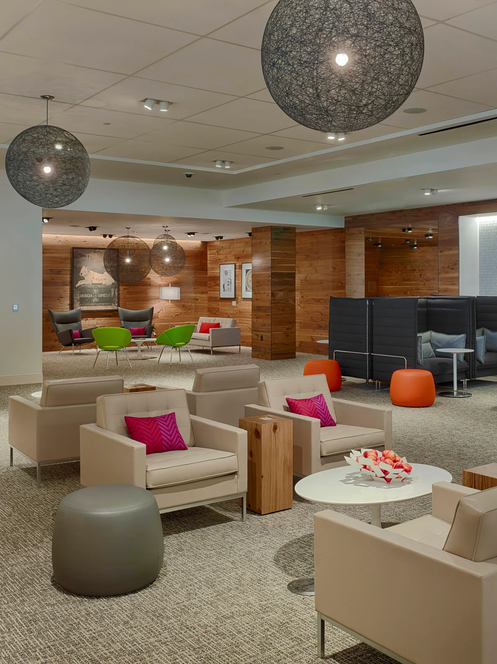 Grey and beige armchairs around round tables under a mesh pendant light against wood paneling in the Centurion Lounge at Houston Intercontinental (IAH).