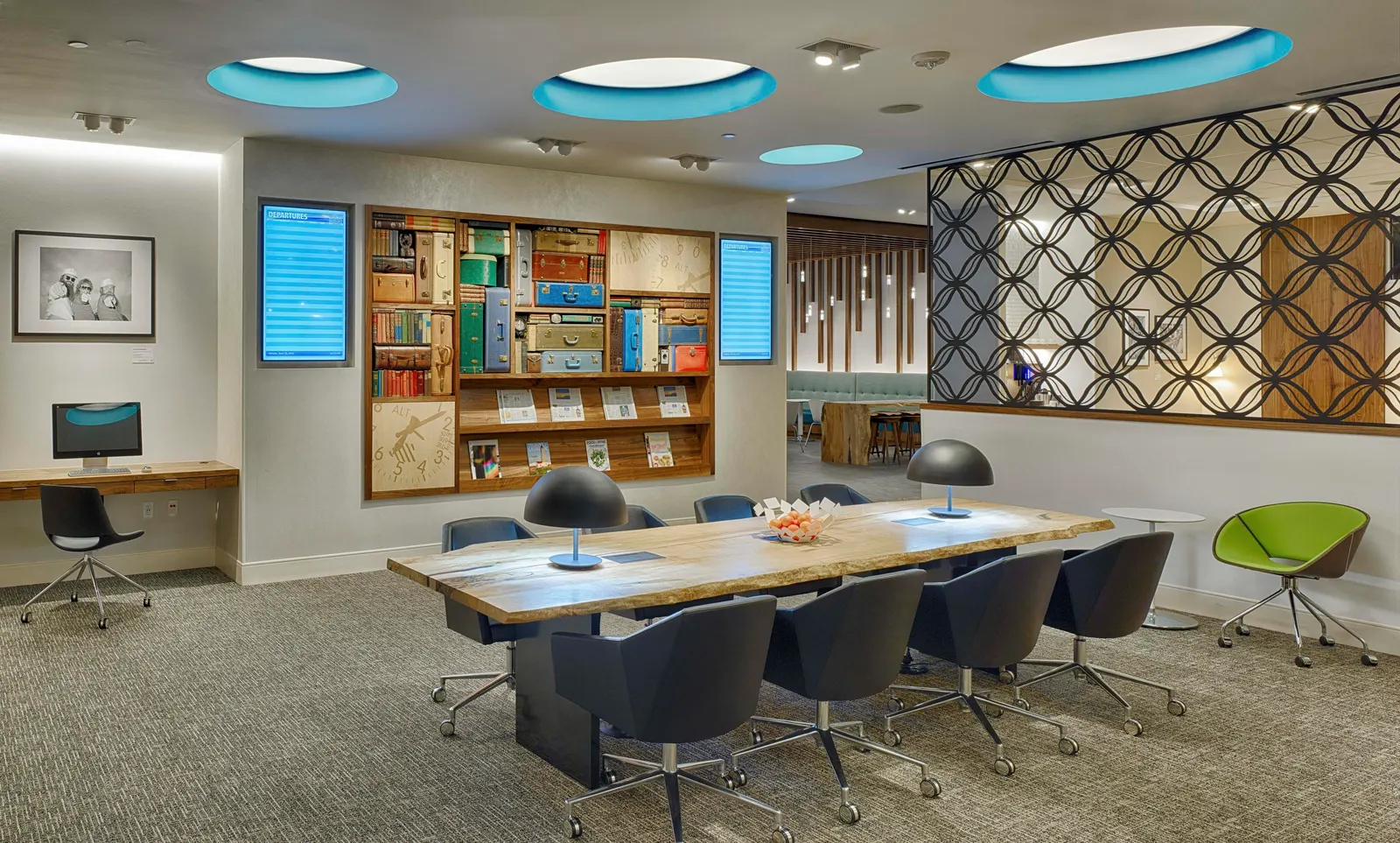 Communal wood work table with navy office chairs in front of a bookcase wall and flight displays in the Centurion Lounge at Houston Intercontinental (IAH).