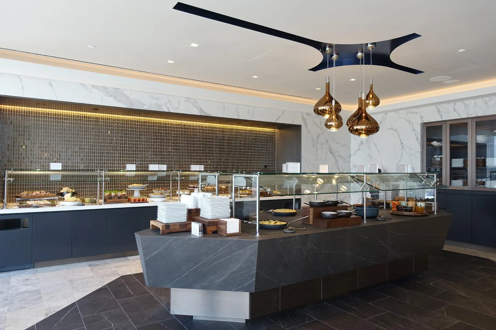 Buffet island with amber pendants and marble back wall in the United Polaris Lounge at Houston Intercontinental (IAH).