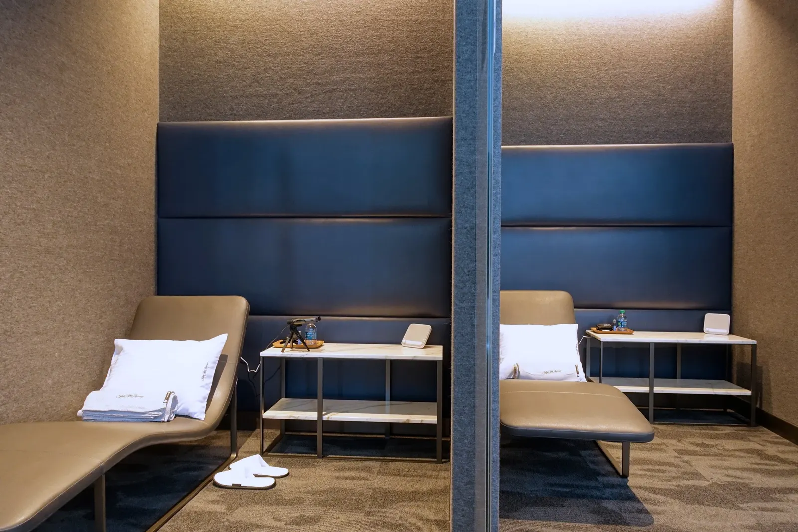 Tan leather chaise nap pods with blue headboards and marble side tables in the United Polaris Lounge at Houston Intercontinental (IAH).
