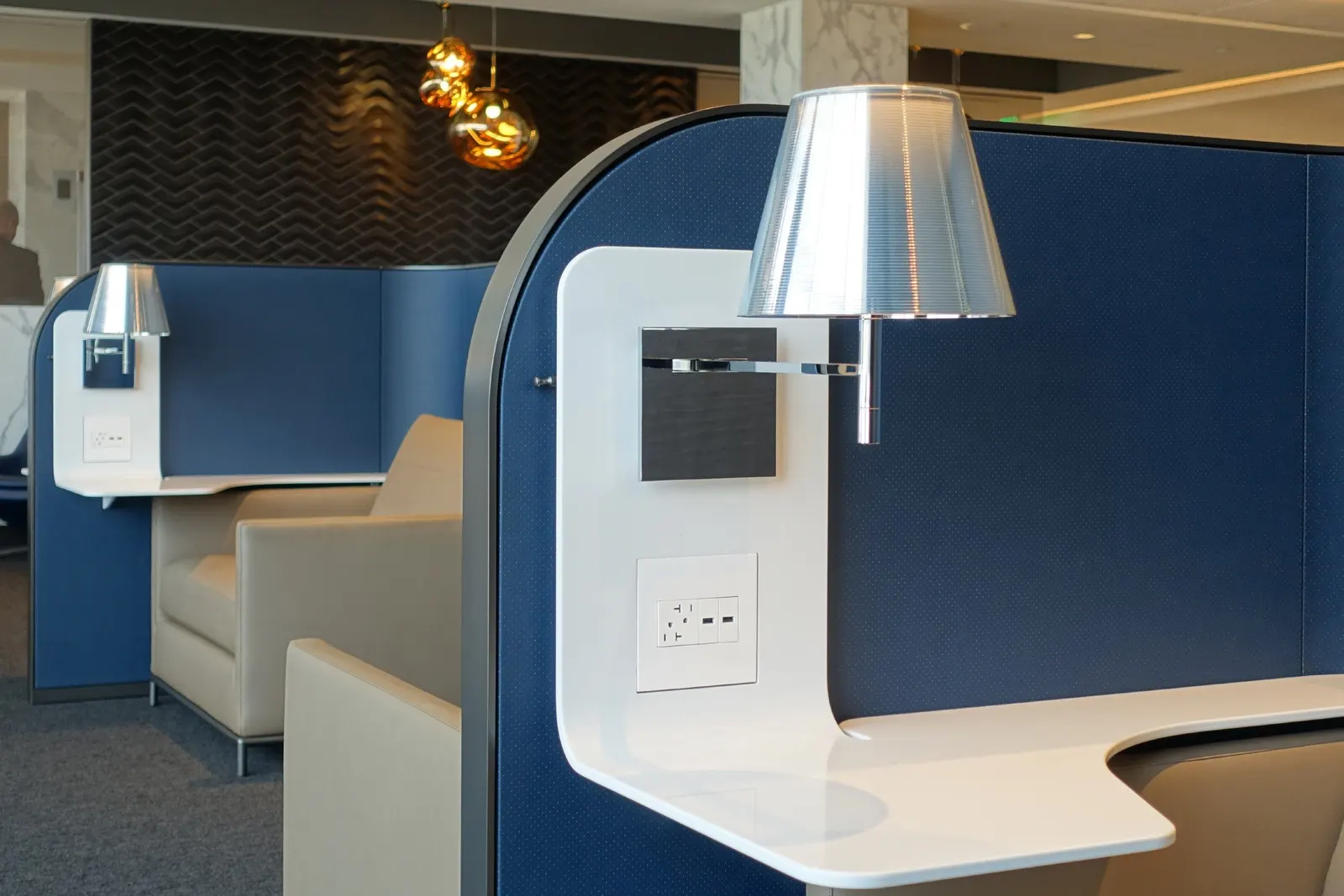 Semi-private seating pods with swing-arm lamps and USB power in the United Polaris Lounge at Houston Intercontinental (IAH).
