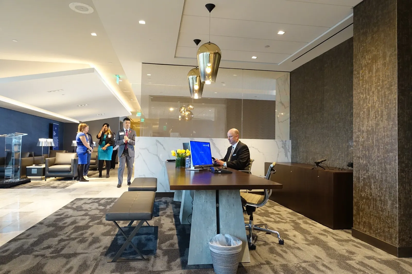 Reception desk with gold pendant lights overlooking lounge seating in the United Polaris Lounge at Houston Intercontinental (IAH).