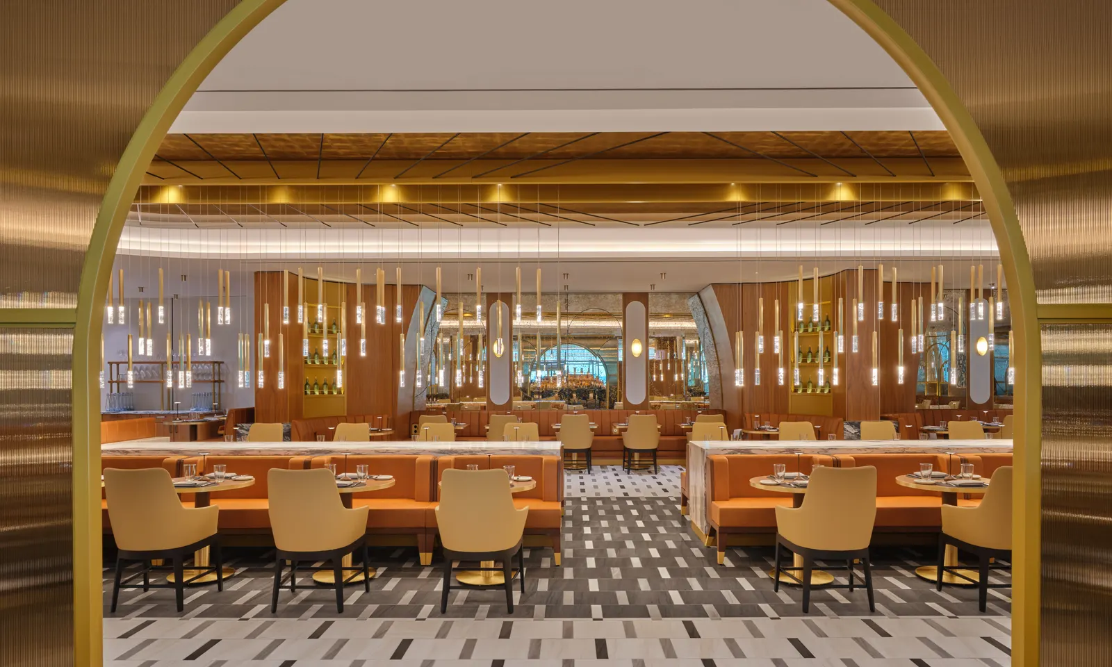 Gold-framed entrance into the Brasserie dining room with orange banquettes and hanging cylinder lights in the Delta One Lounge at New York JFK Terminal 4.